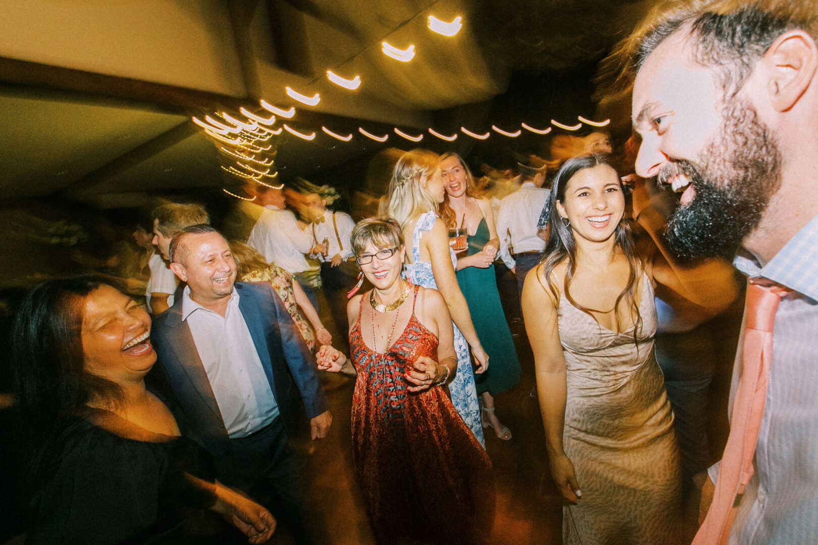 A joyous group of people smiling and dancing under dim lights at a Normandy Farm Wedding. The slightly blurred image perfectly captures the lively atmosphere and motion.