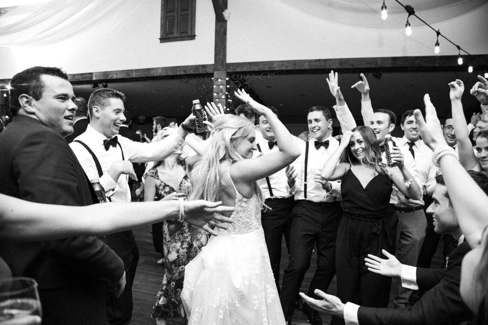 At a vibrant Normandy Farm Wedding, the bride dances joyfully among her guests. The group is smiling, raising their hands in celebration, creating a scene of pure happiness and unity.