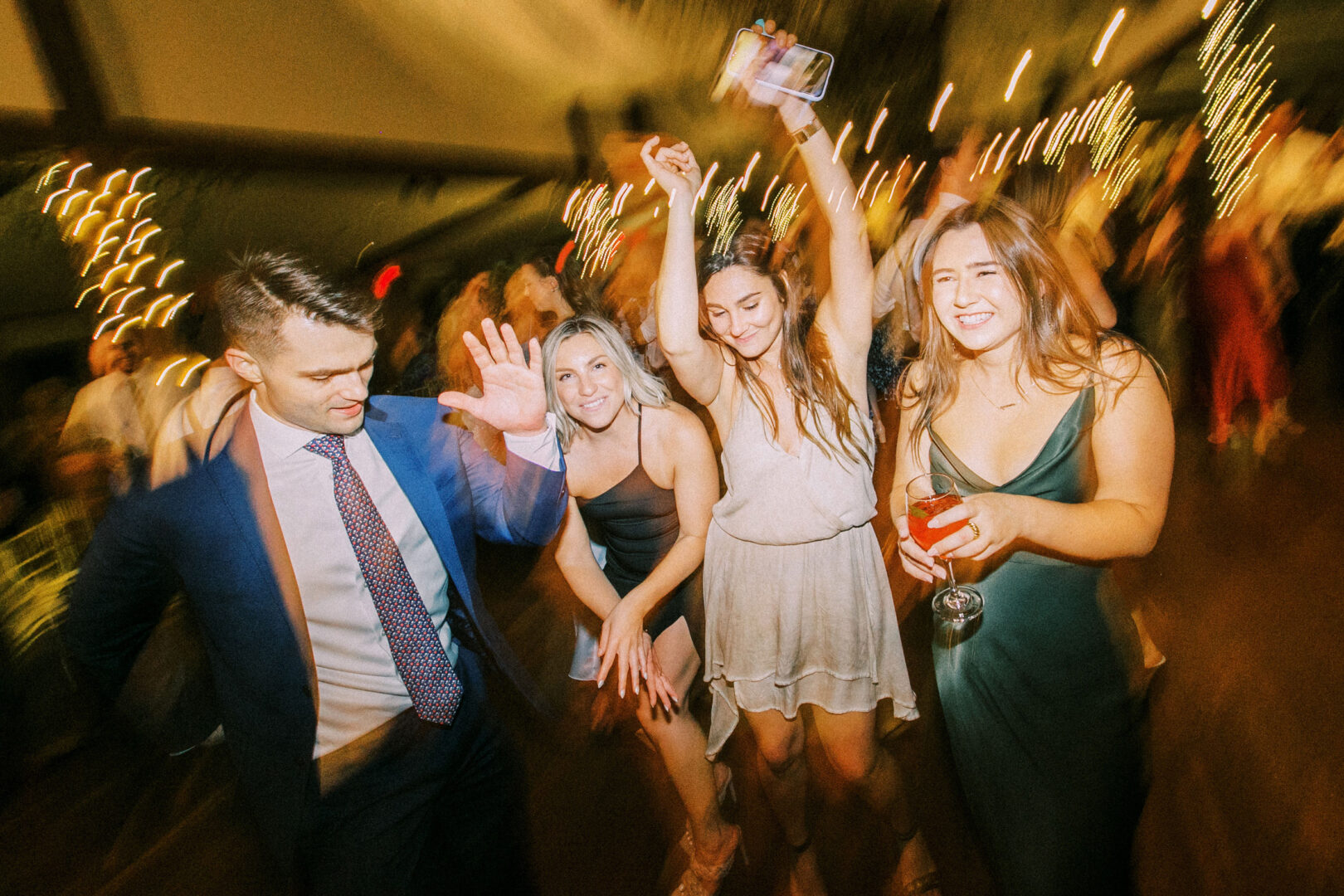 People dancing and enjoying a Normandy Farm wedding, with colorful lights and blurred motion effects setting the perfect celebratory vibe.