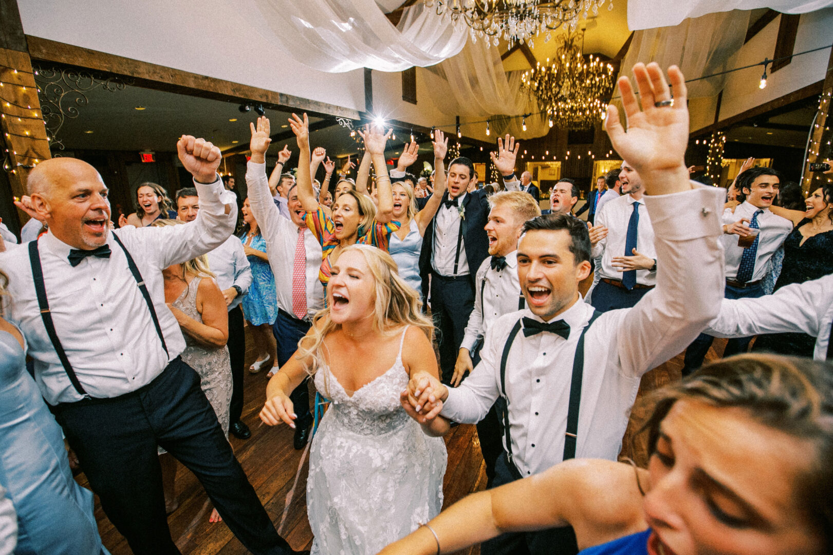 At a cheerful Normandy Farm Wedding, the joyful bride and groom celebrate while dancing with guests at a festive indoor reception.