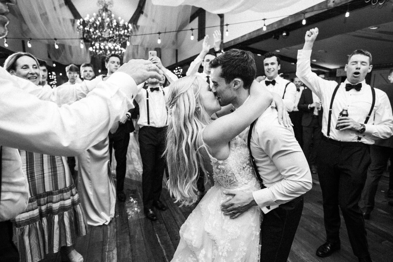 At a picturesque Normandy Farm Wedding, the bride and groom share a tender kiss on the dance floor, surrounded by cheering guests at the reception.