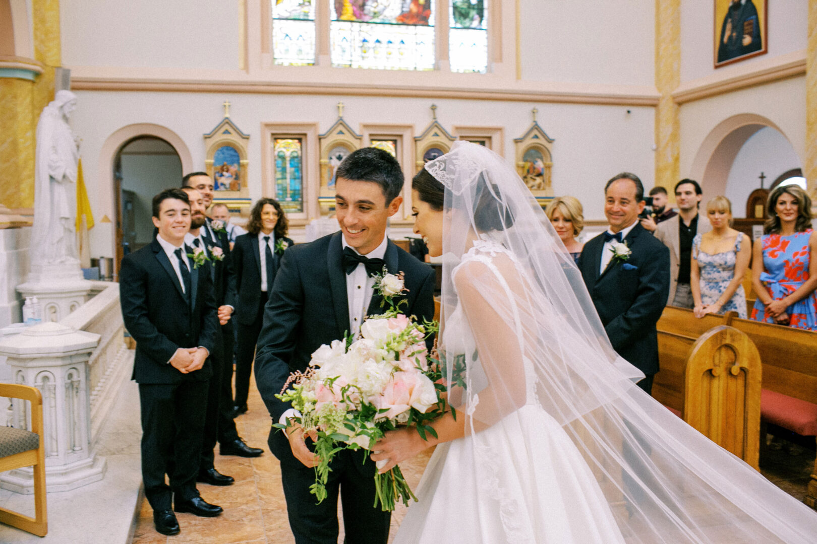 A bride and groom stand at the altar in a church, reminiscent of a Cape May Convention Hall wedding. The bride holds a bouquet, both smiling brightly. The groom wears a black tuxedo, while the bride is stunning in her white gown, with guests joyfully seated in the background.