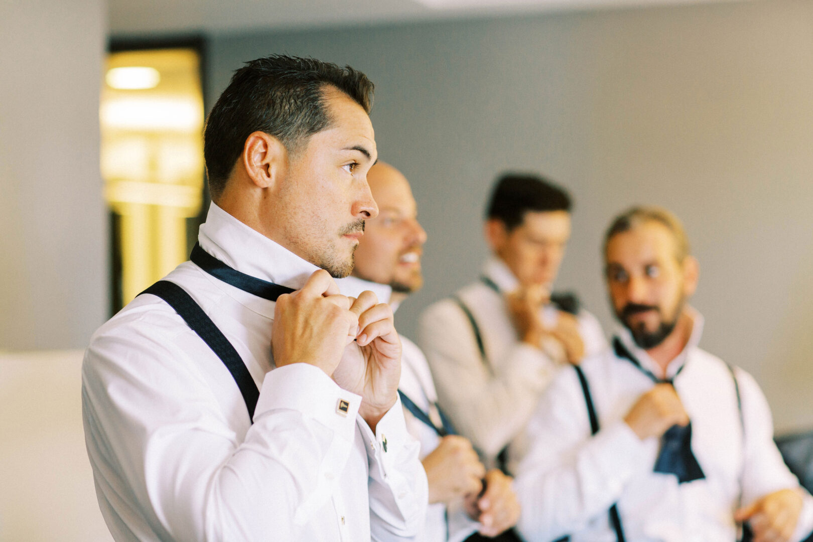 In a room at the Mansion on Main Street, four men in white shirts and suspenders adjust their ties, preparing for the wedding photos.