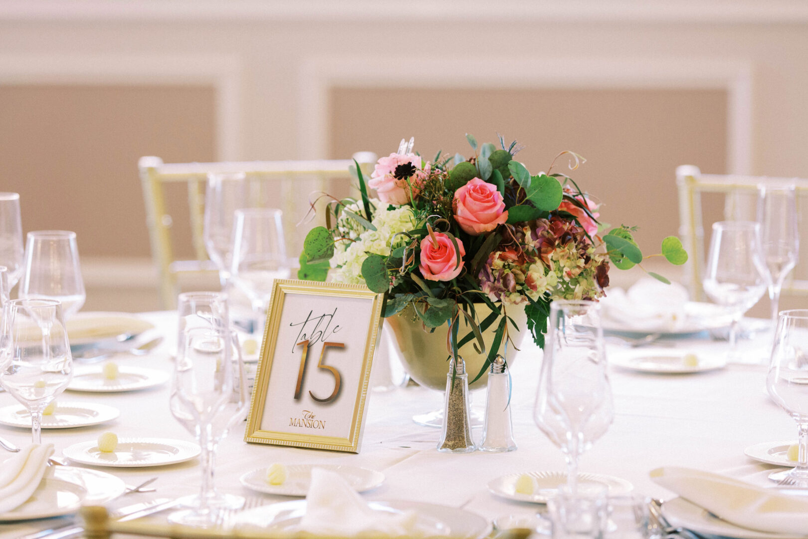 Elegant table setting at the Mansion on Main Street, complete with a floral centerpiece, table number 15, multiple wine glasses, and butter dishes—perfect for unforgettable wedding photos.