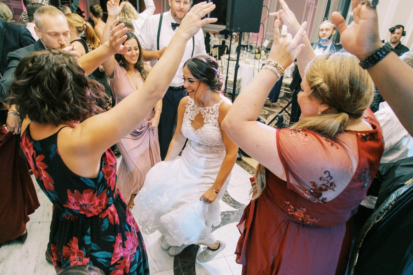 A bride in a white dress dances joyfully at the Mansion on Main Street, surrounded by guests in colorful attire, creating perfect wedding photos and an unforgettable celebration.