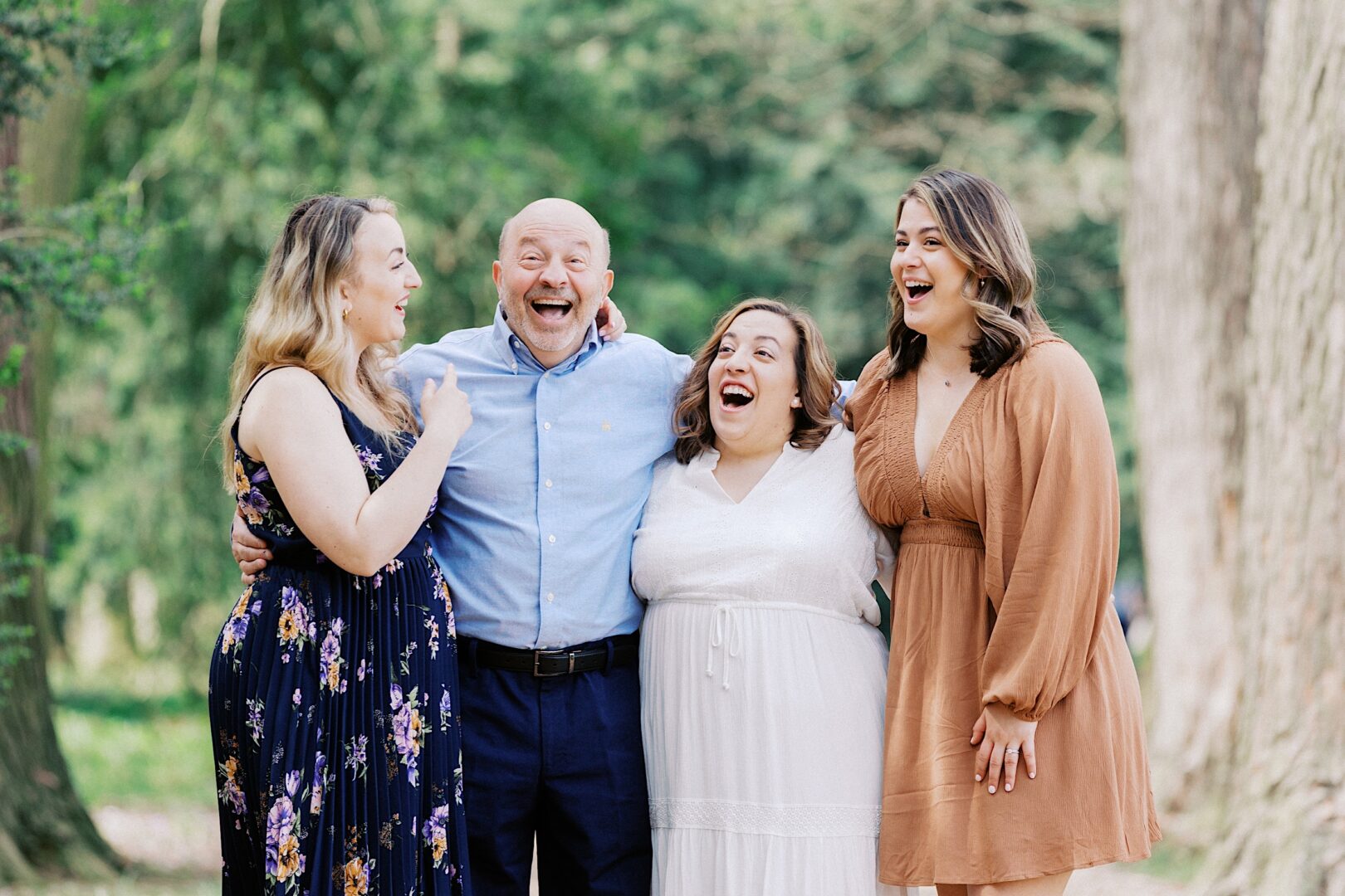 Four people stand outdoors, smiling and laughing together among tall trees—a perfect backdrop for spring family photos.