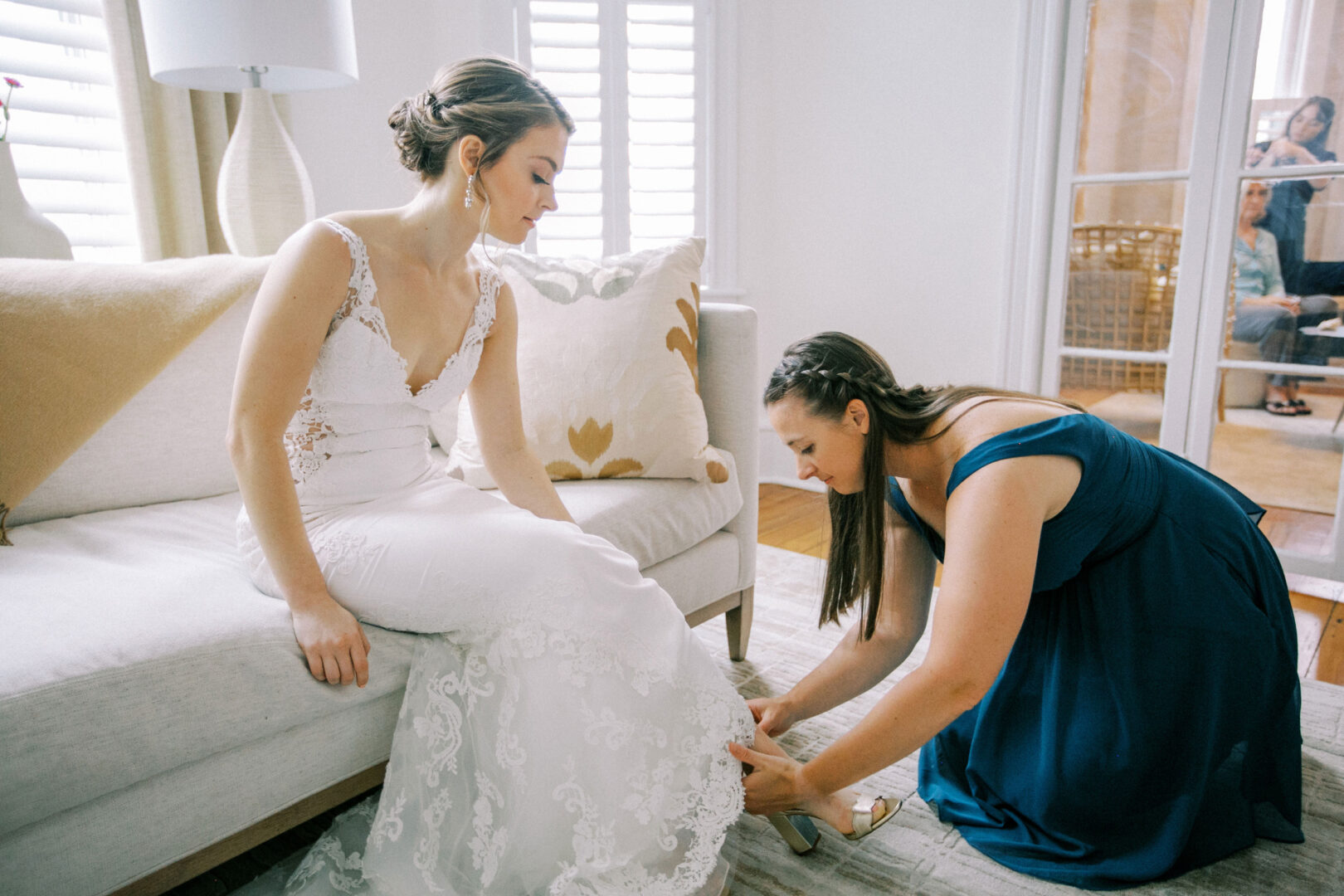 Bridesmaid helps the bride put her shoes on at the start of the Cape May wedding day.