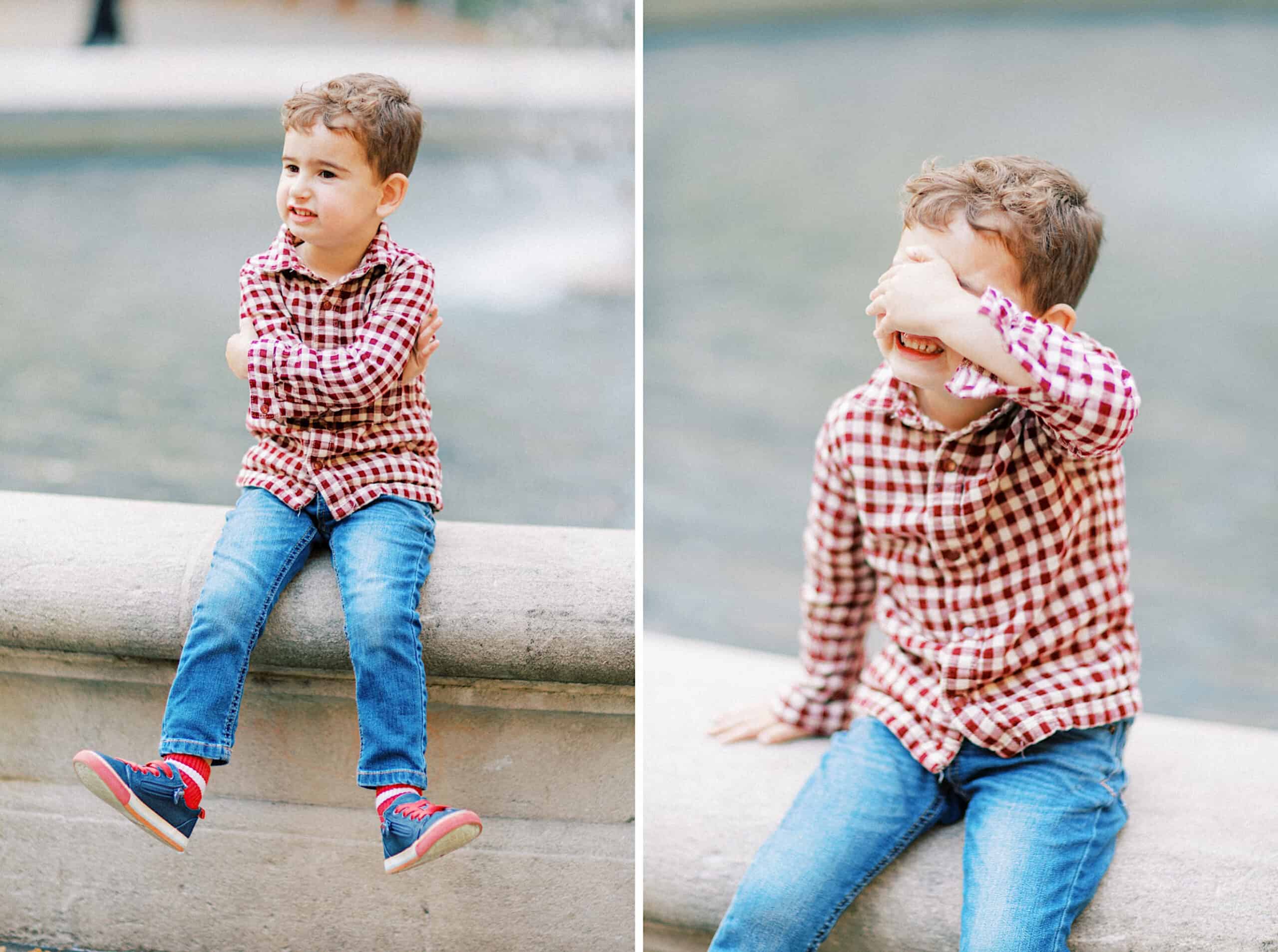 A young boy in a red plaid shirt and jeans sits on a stone ledge near water during family photos at Washington Square in Philadelphia; in one image, he crosses his arms, while in the other, he covers his face with his hand.