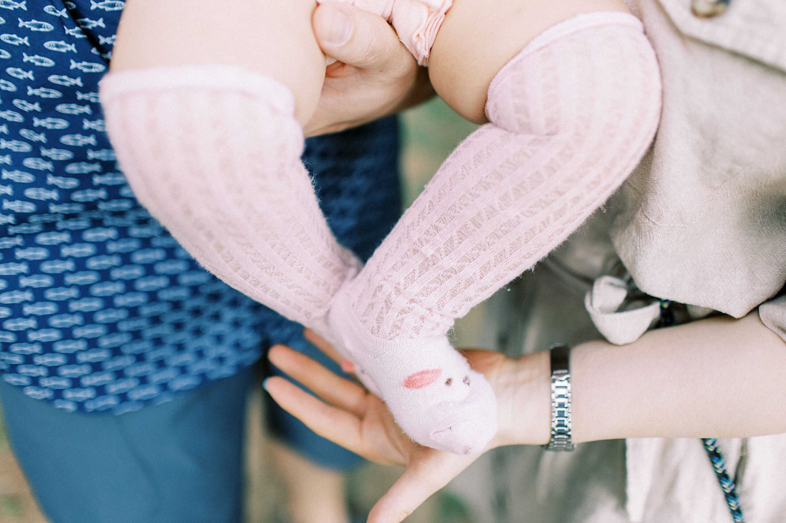 Close-up of an adult holding a baby in pink textured knee-high socks with a small animal face design, perfect for maternity and extended family photos.