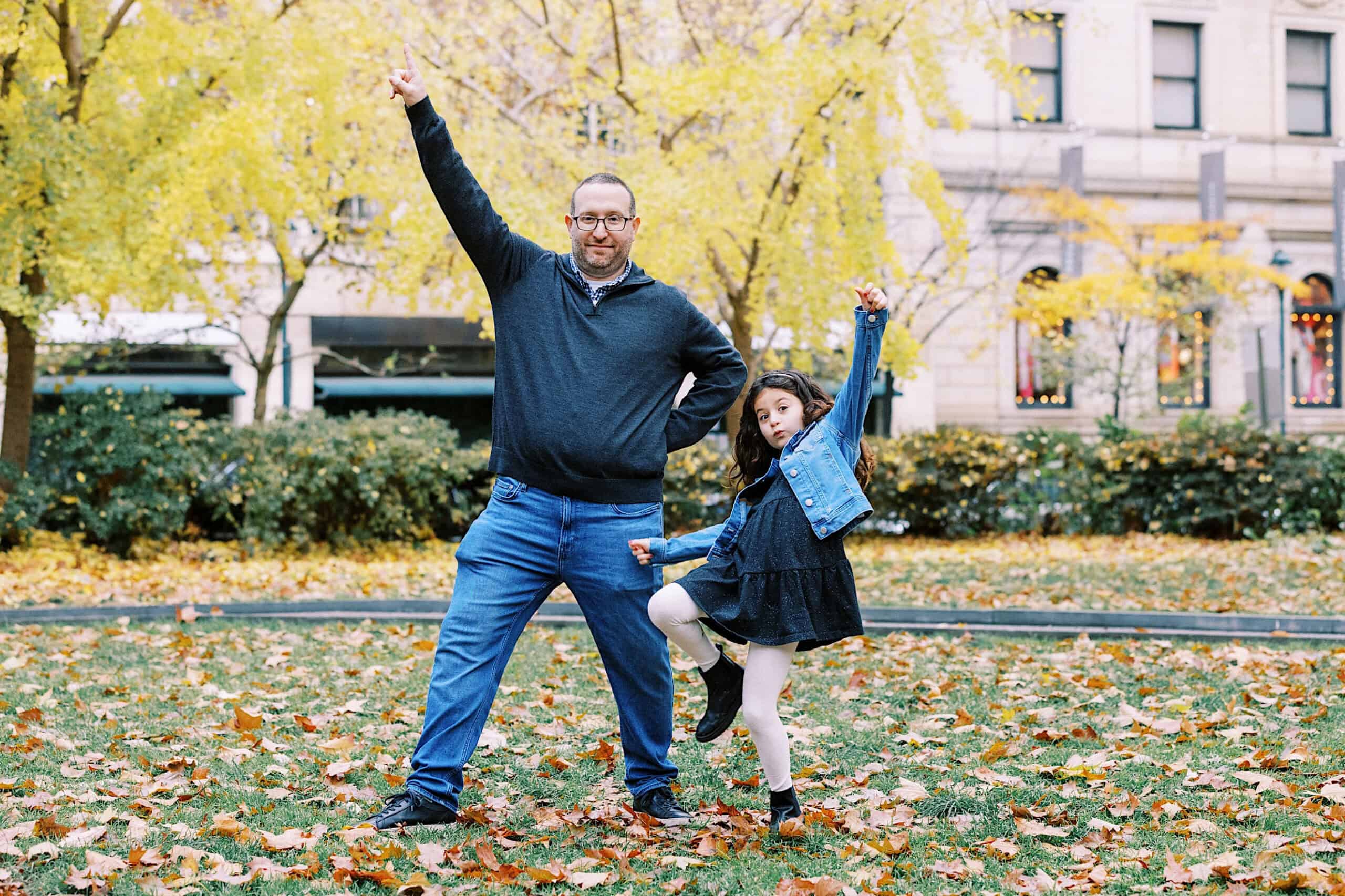 An adult man and a young girl strike playful poses together among autumn leaves in Rittenhouse Square, capturing the perfect moment for Fall Family Photos.