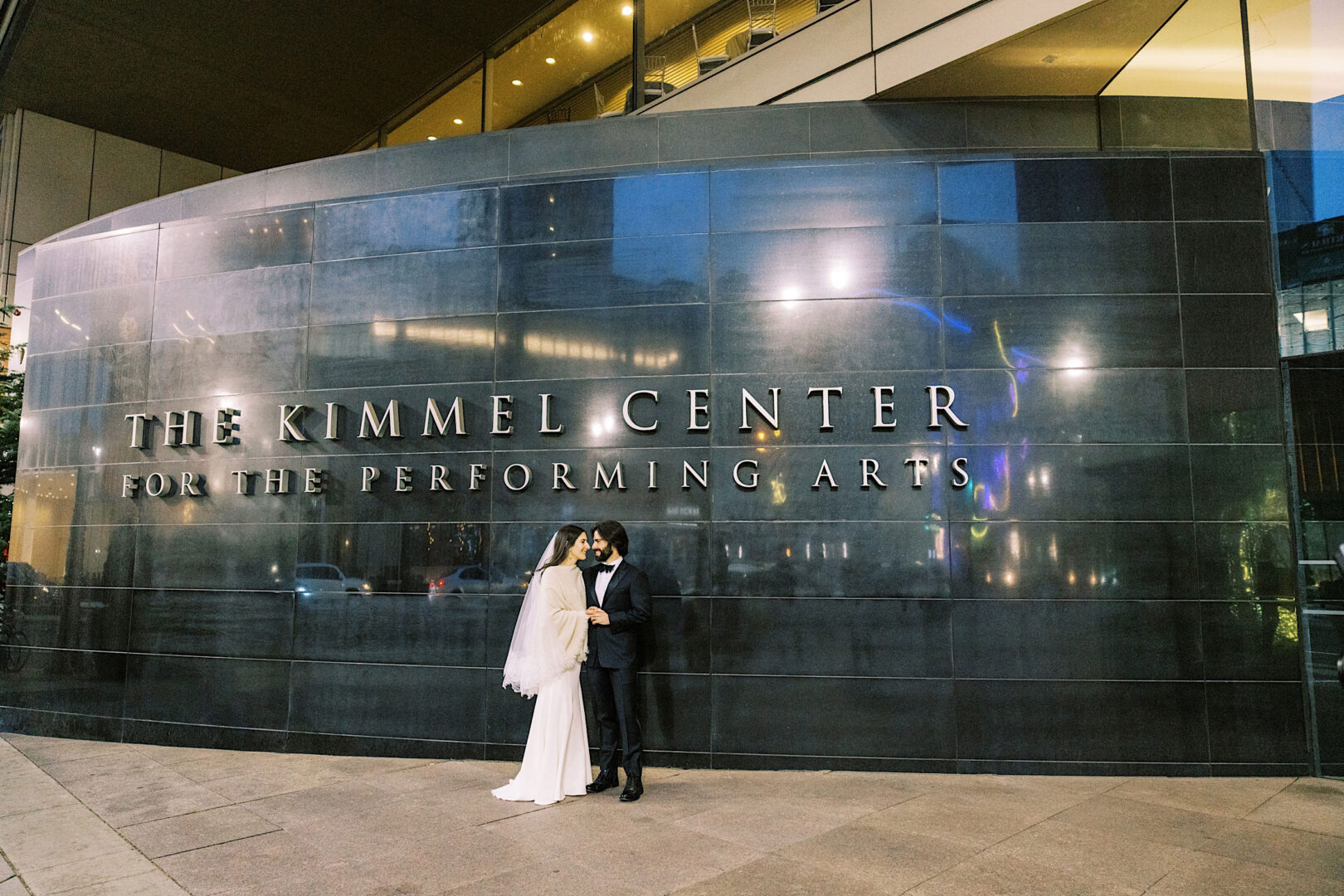 A bride and groom stand in front of the Kimmel Center in Philadelphia, capturing their wedding day's essence.