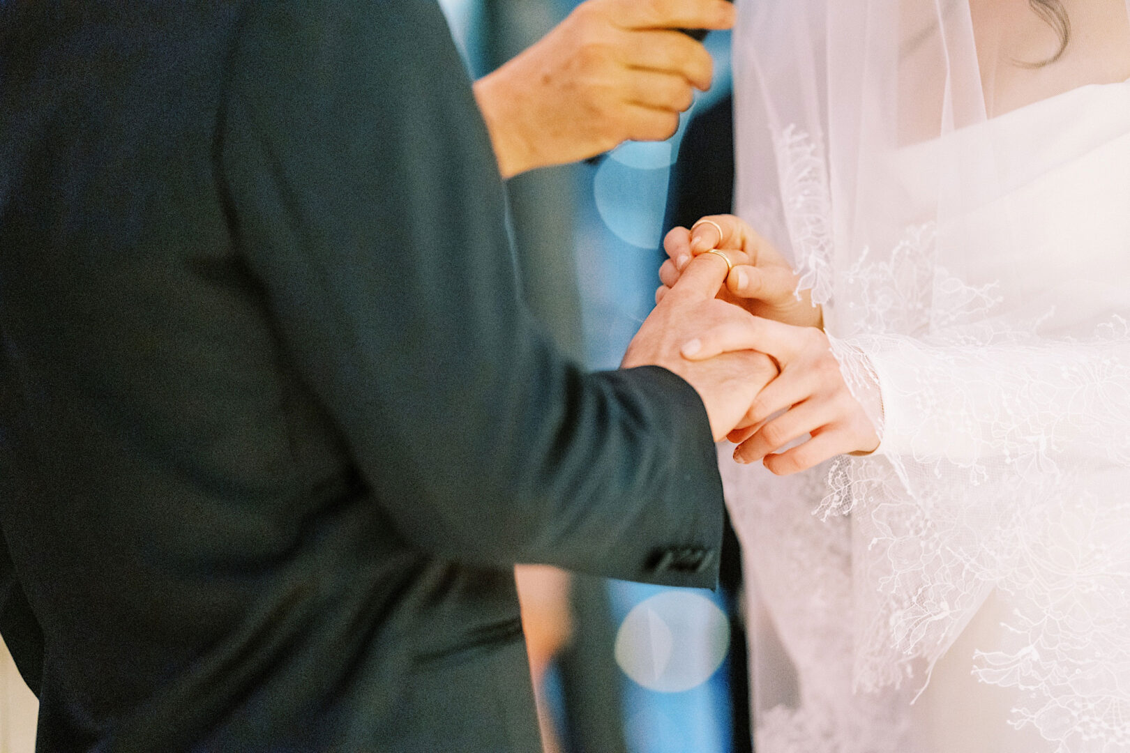 Close-up of a couple exchanging rings during their wedding ceremony at the Kimmel Center in Philadelphia. The bride's hand is adorned with lace, while the groom wears a dark suit.