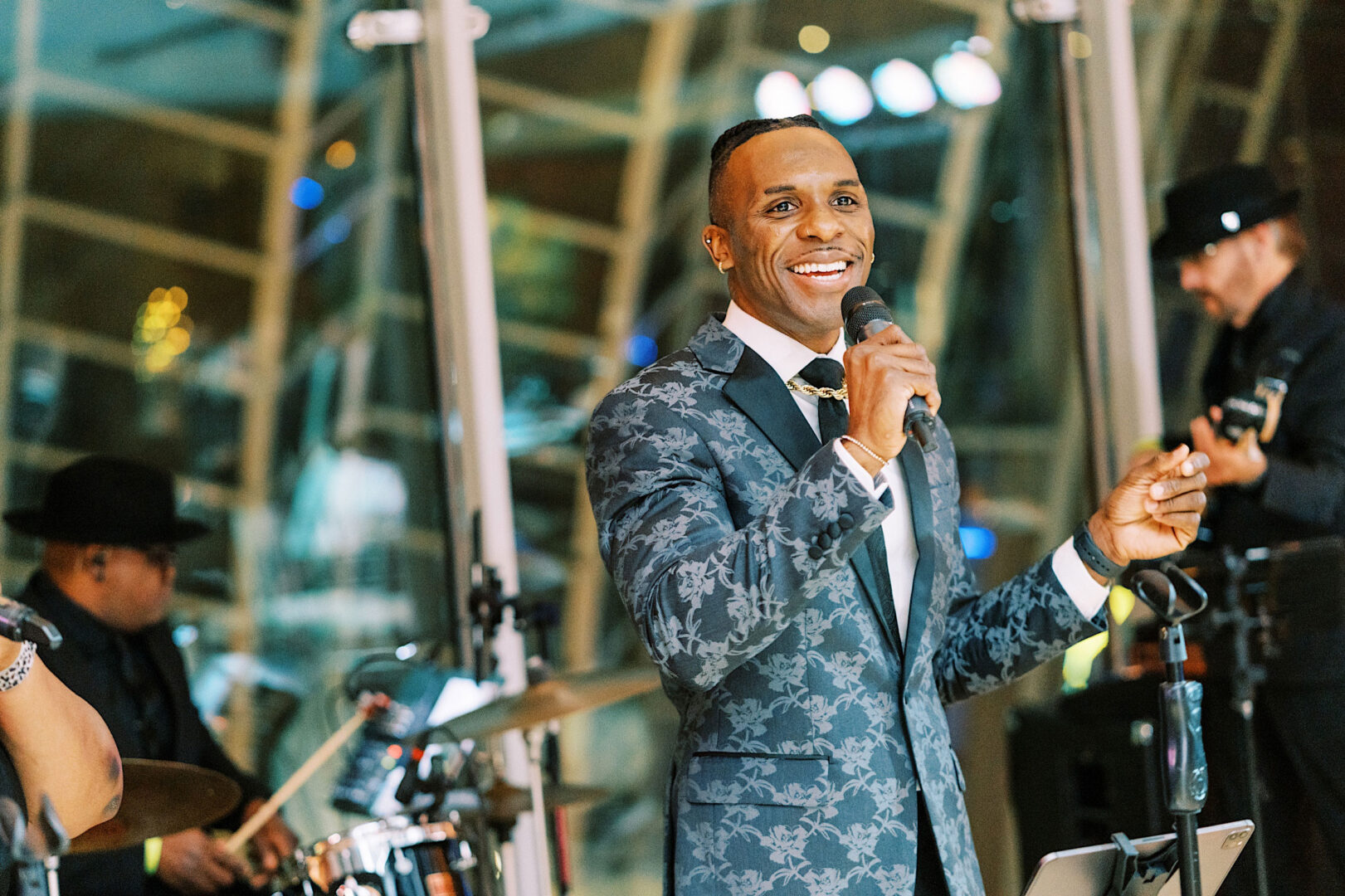 A man in a patterned suit holds a microphone and sings on stage with a band in the background, celebrating New Year's Eve at the Kimmel Center.