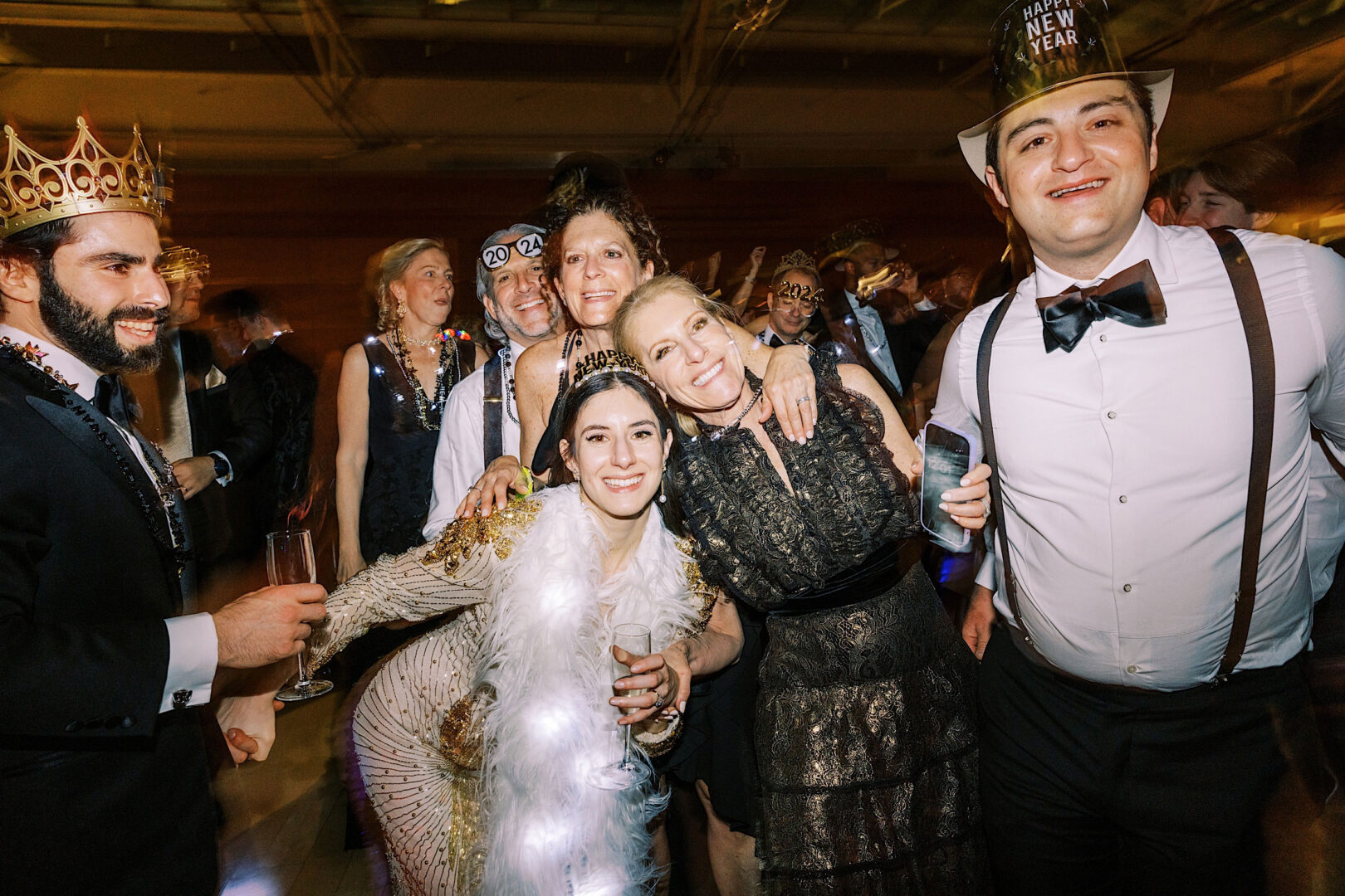 A group of people dressed in formal and festive attire celebrate a New Year's Eve party at the Kimmel Center, with hats and decorations commemorating the year 2020.
