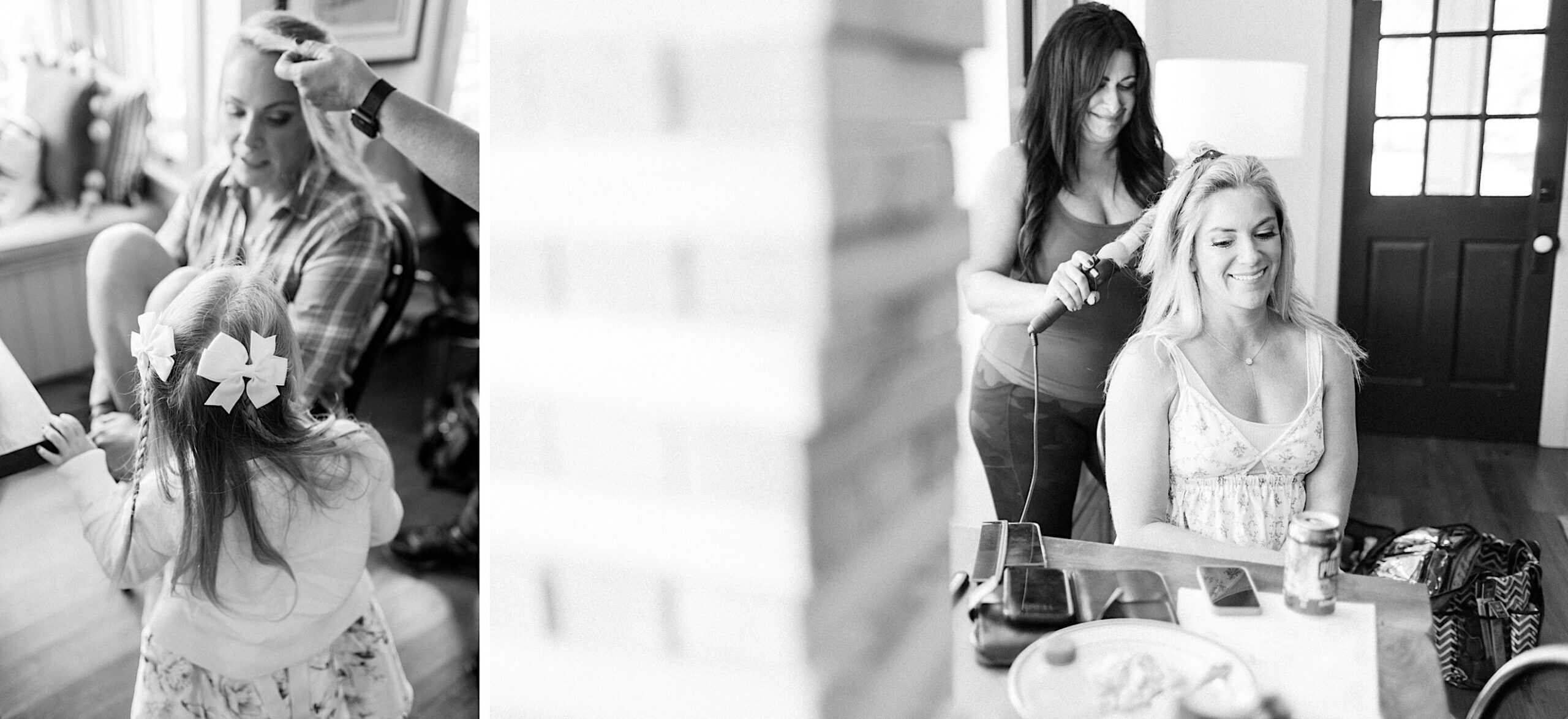 Two women have their hair styled indoors as they prepare for a Beach Plum Farm Wedding; a young girl with bows in her hair is also present. The casual, relaxed setting includes everyday items scattered across the table.