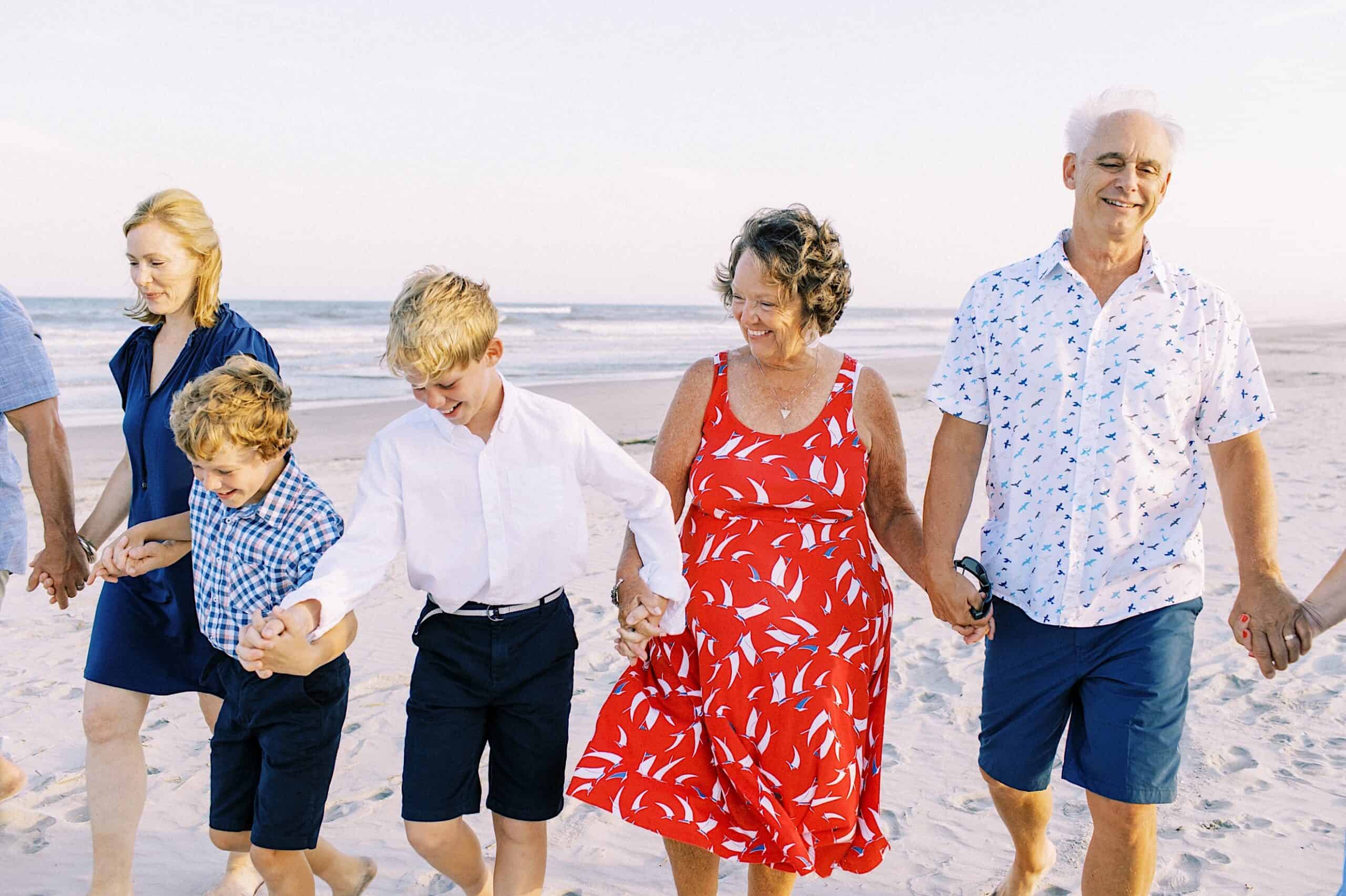 A group of people, including two children and three adults, walk hand in hand along a sandy beach by the ocean, capturing the essence of Jersey Shore family photos.