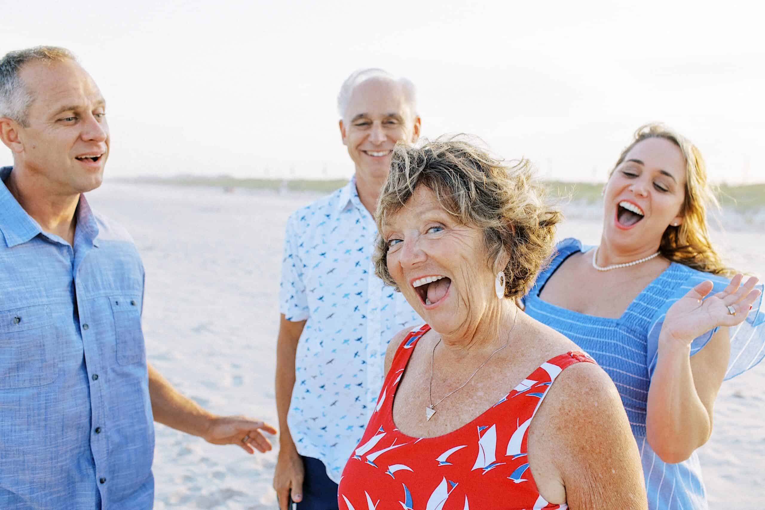 Four adults stand on a sandy beach, smiling and laughing together. The sky is clear and bright in the background, creating the perfect setting for memorable Jersey Shore family photos.