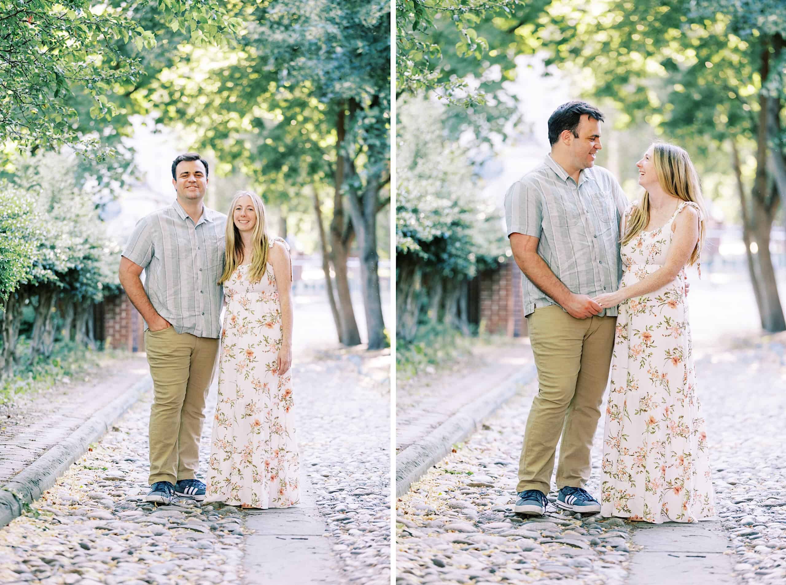 A man and woman stand together on a cobblestone path lined with trees, holding hands and smiling at each other in one of the two side-by-side Old City Philadelphia engagement photos.
