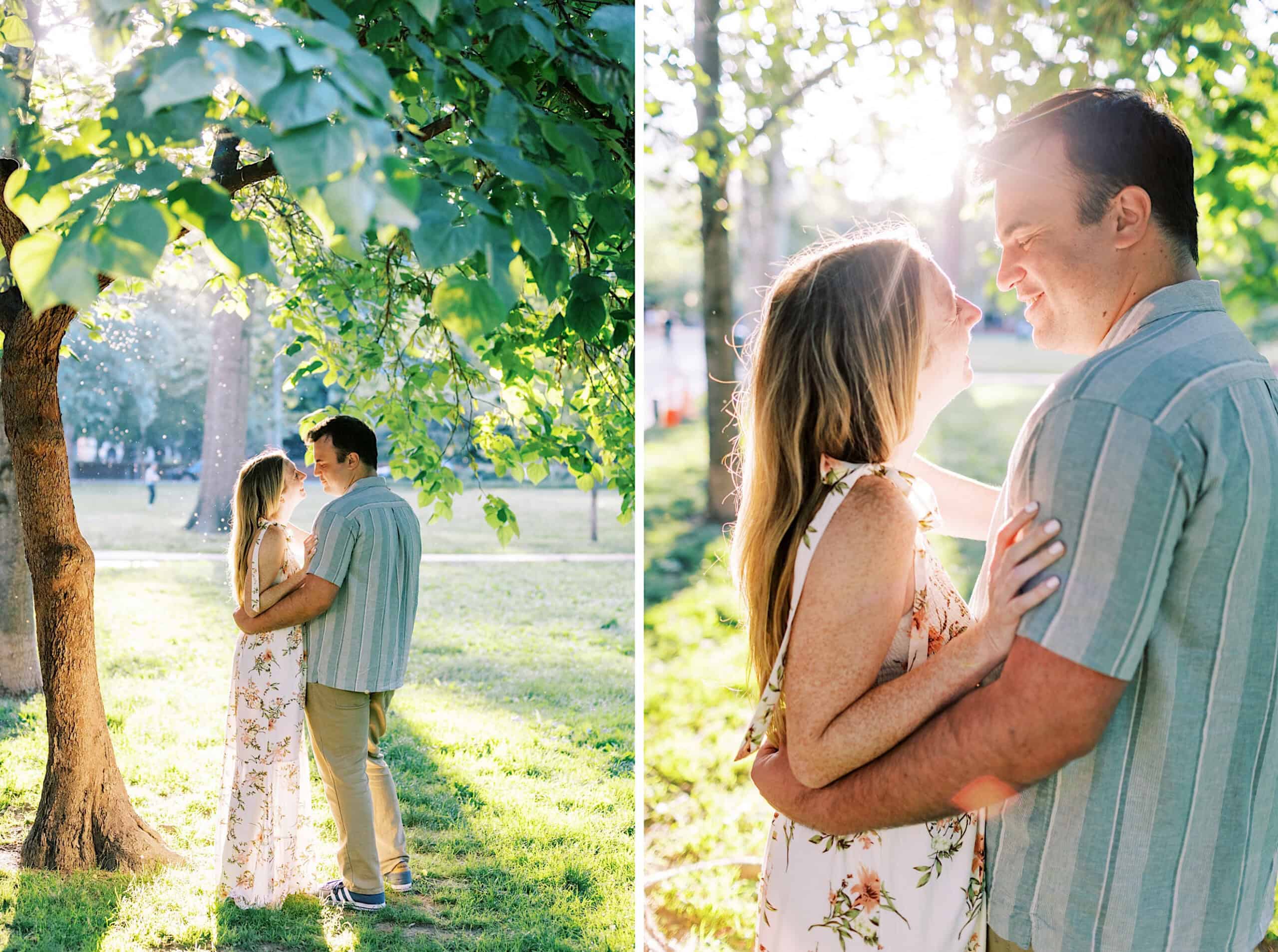 A couple stands closely together in a sunlit park, surrounded by green trees and grass, smiling at each other during their Old City Philadelphia engagement photos.