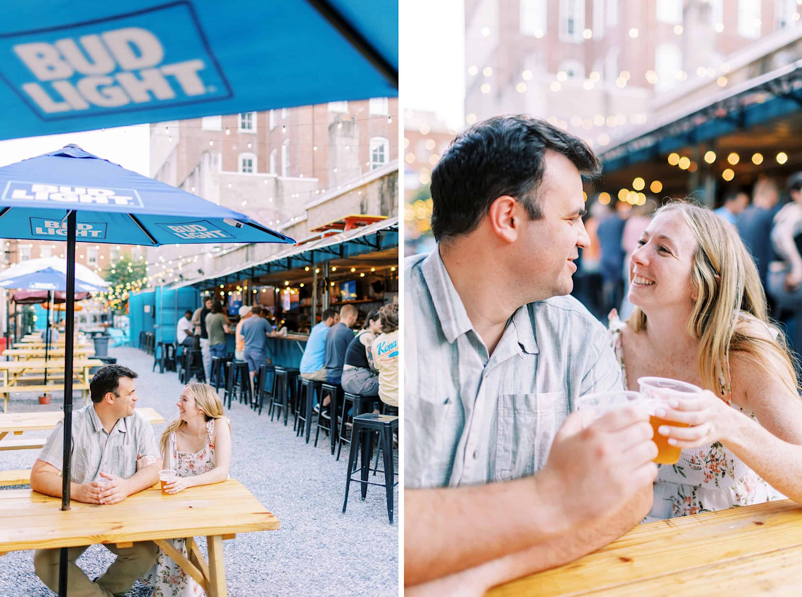 A couple sits at a wooden table with drinks under a Bud Light umbrella in an outdoor bar area; most seats are occupied, string lights hang above—perfect for candid Old City Philadelphia engagement photos.