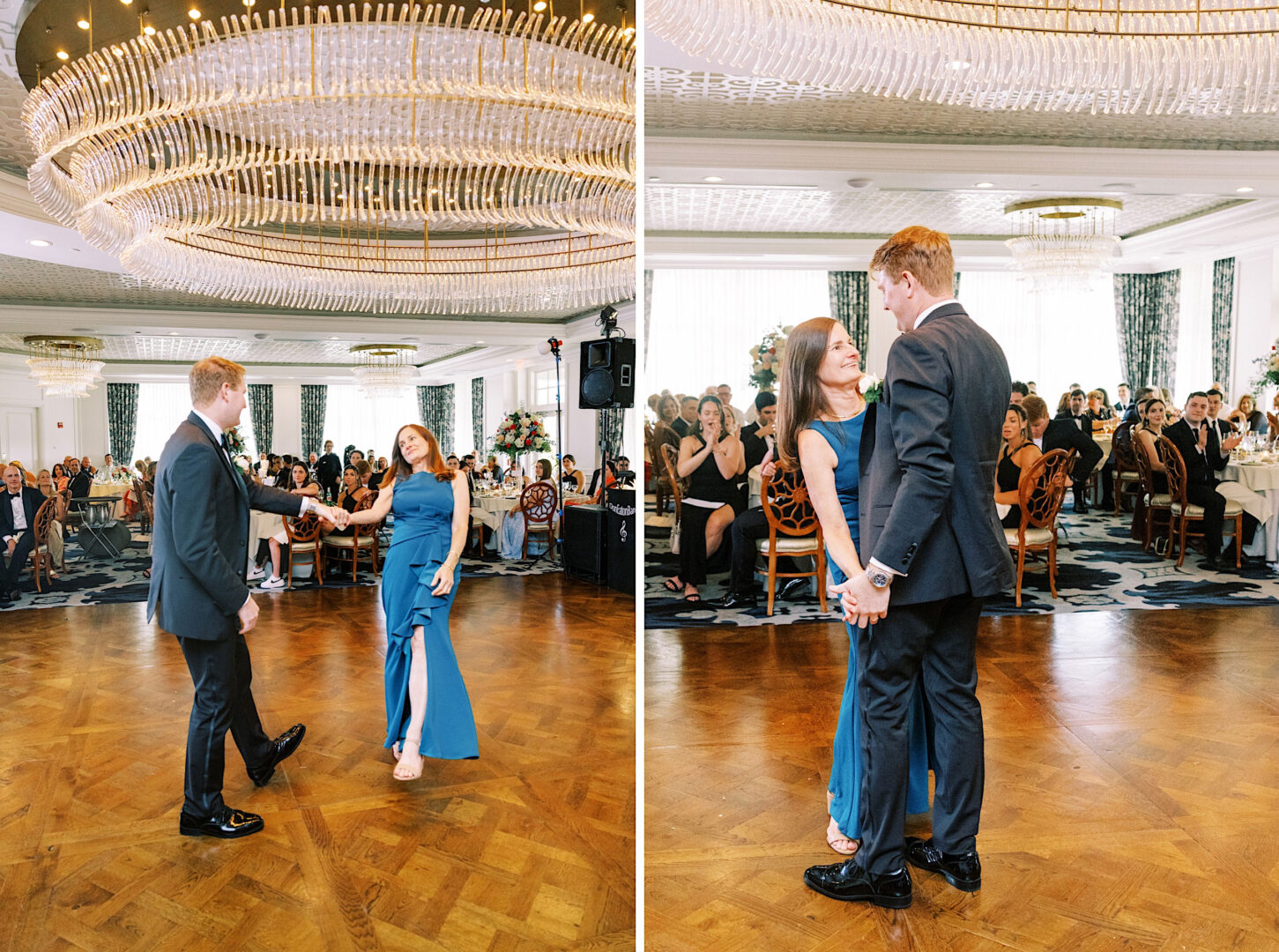 A couple dances in a formal ballroom at the Overbrook Golf Club Wedding, with a large chandelier above and an audience seated at round dining tables watching them. The woman is in a blue dress and the man is in a black suit.