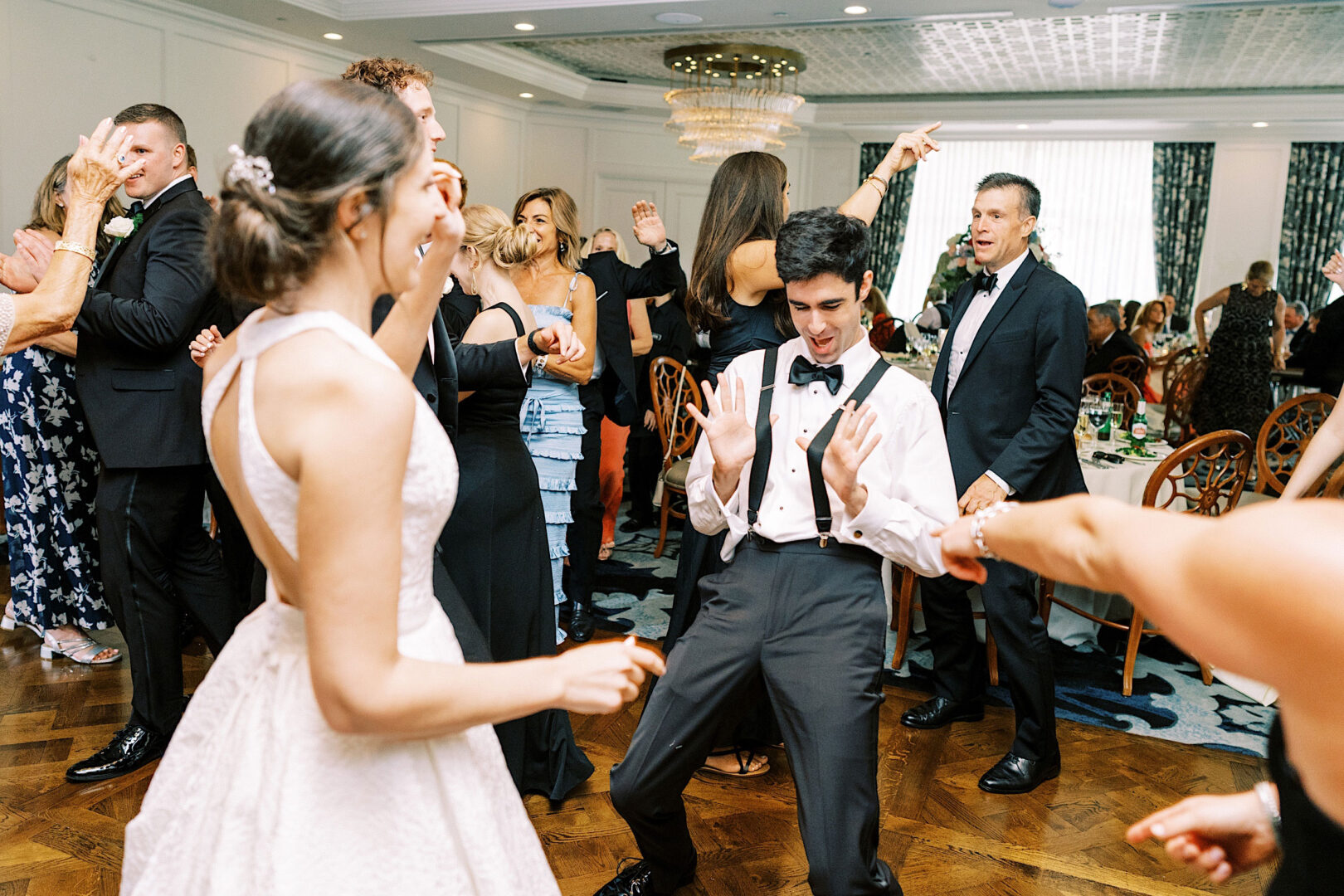 People dressed in formal attire are dancing energetically at a lively event in a well-decorated indoor venue, celebrating an Overbrook Golf Club Wedding near Villanova.