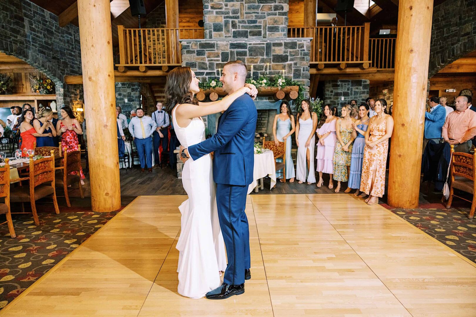 A bride and groom share their first dance in a large, rustic venue with wooden beams and stone walls at The Ridge at Back Brook, surrounded by guests celebrating their New Jersey wedding.