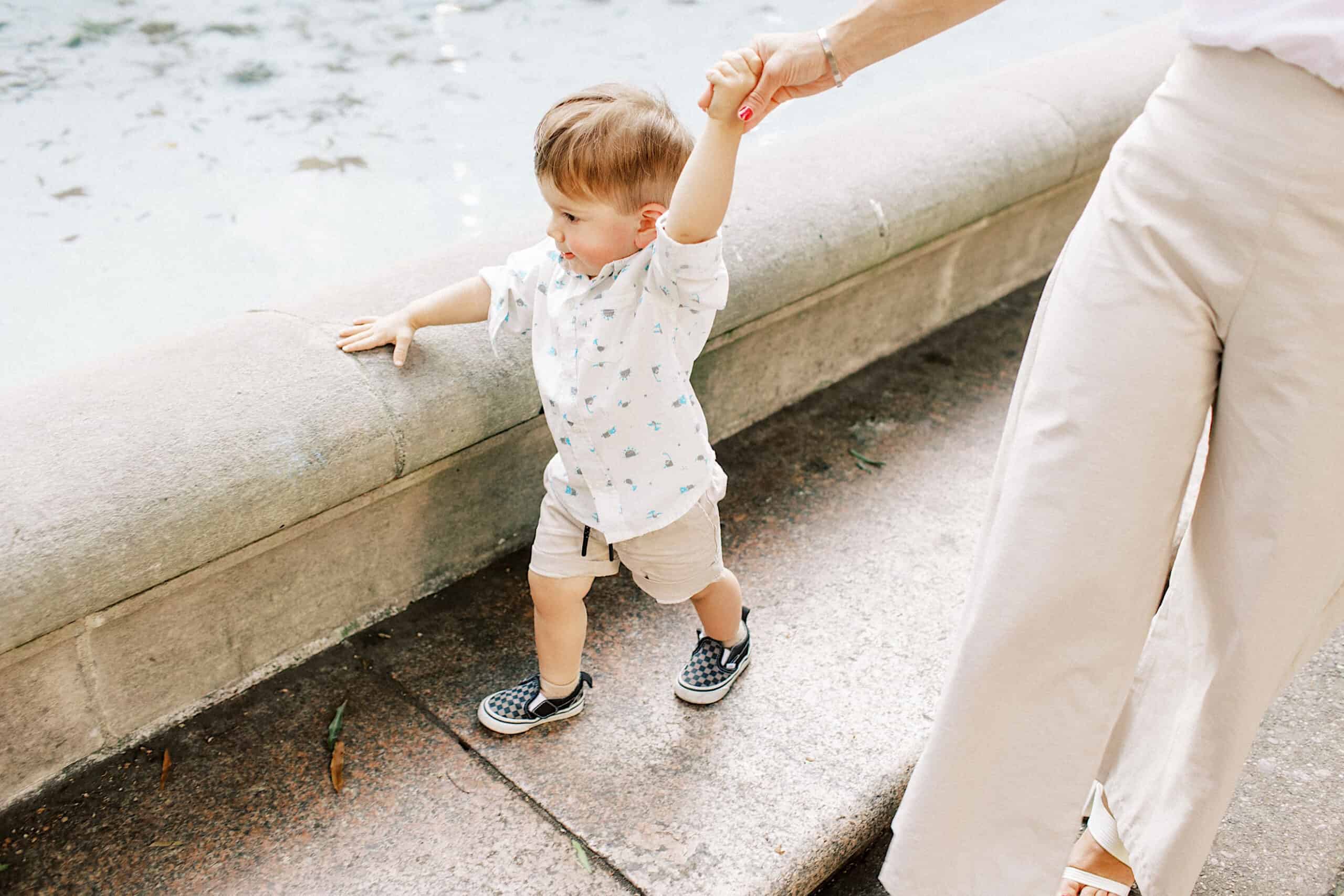A young child walks beside a concrete ledge, holding an adult's hand for support near a body of water—perfect for capturing family photos at Rittenhouse Square.