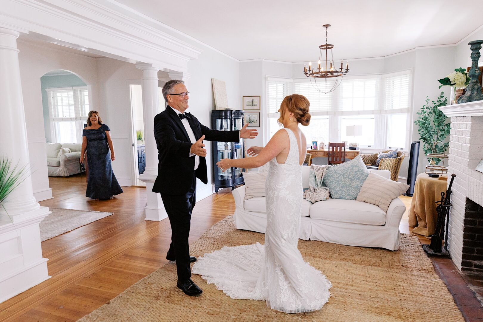 A bride in a white dress and a man in a suit share an embrace at their Corinthian Yacht Club of Cape May wedding ceremony, as another guest stands quietly in the background.