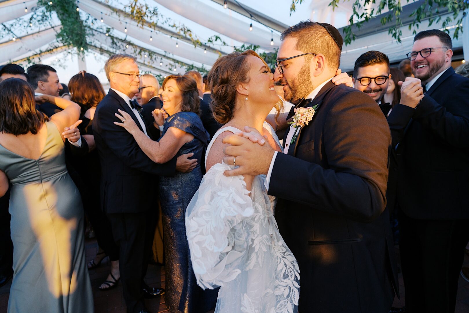 At a Corinthian Yacht Club of Cape May wedding, the bride and groom share a dance at the reception, surrounded by guests dancing under a beautifully decorated canopy.