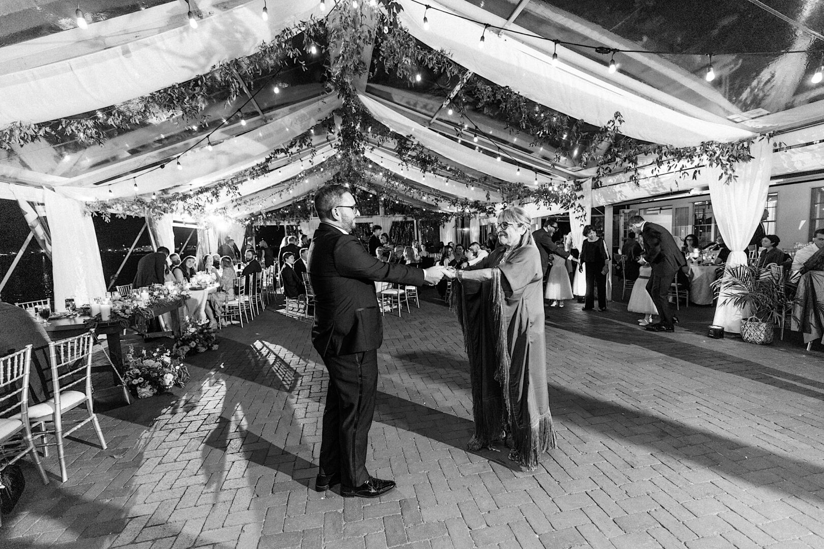 A couple dances under a clear, decorated tent at an evening event at the Corinthian Yacht Club of Cape May Wedding, surrounded by guests seated at tables.