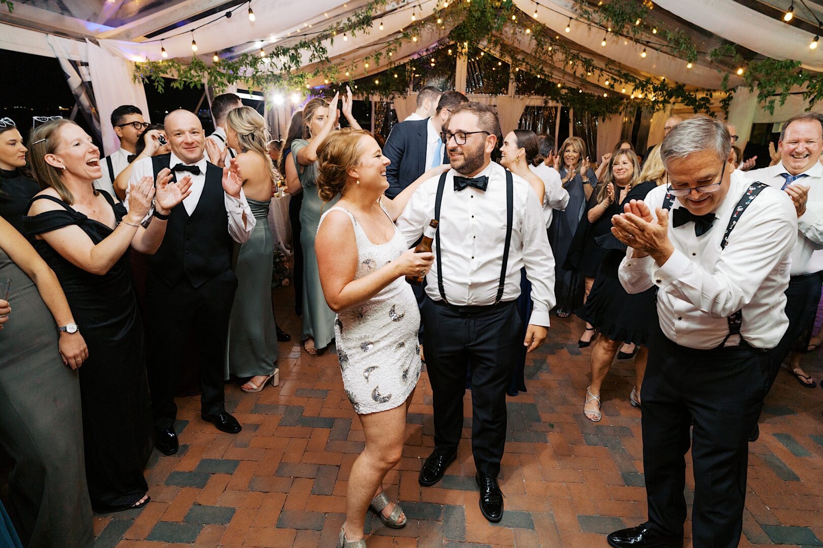 A couple dances happily at a festive Corinthian Yacht Club of Cape May wedding, surrounded by clapping guests under a decorated tent.