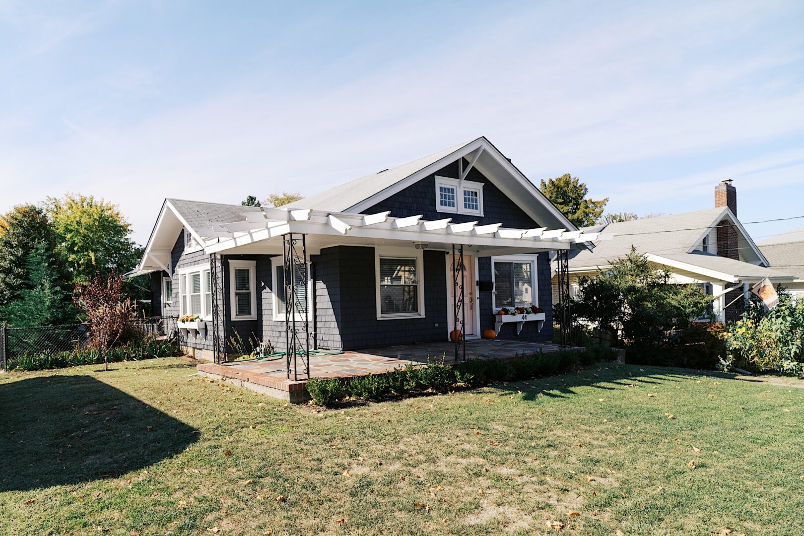 The Tilling House wedding venue boasts a charming single-story house with a gray exterior, white trim, and a pergola-covered porch nestled in a grassy yard.