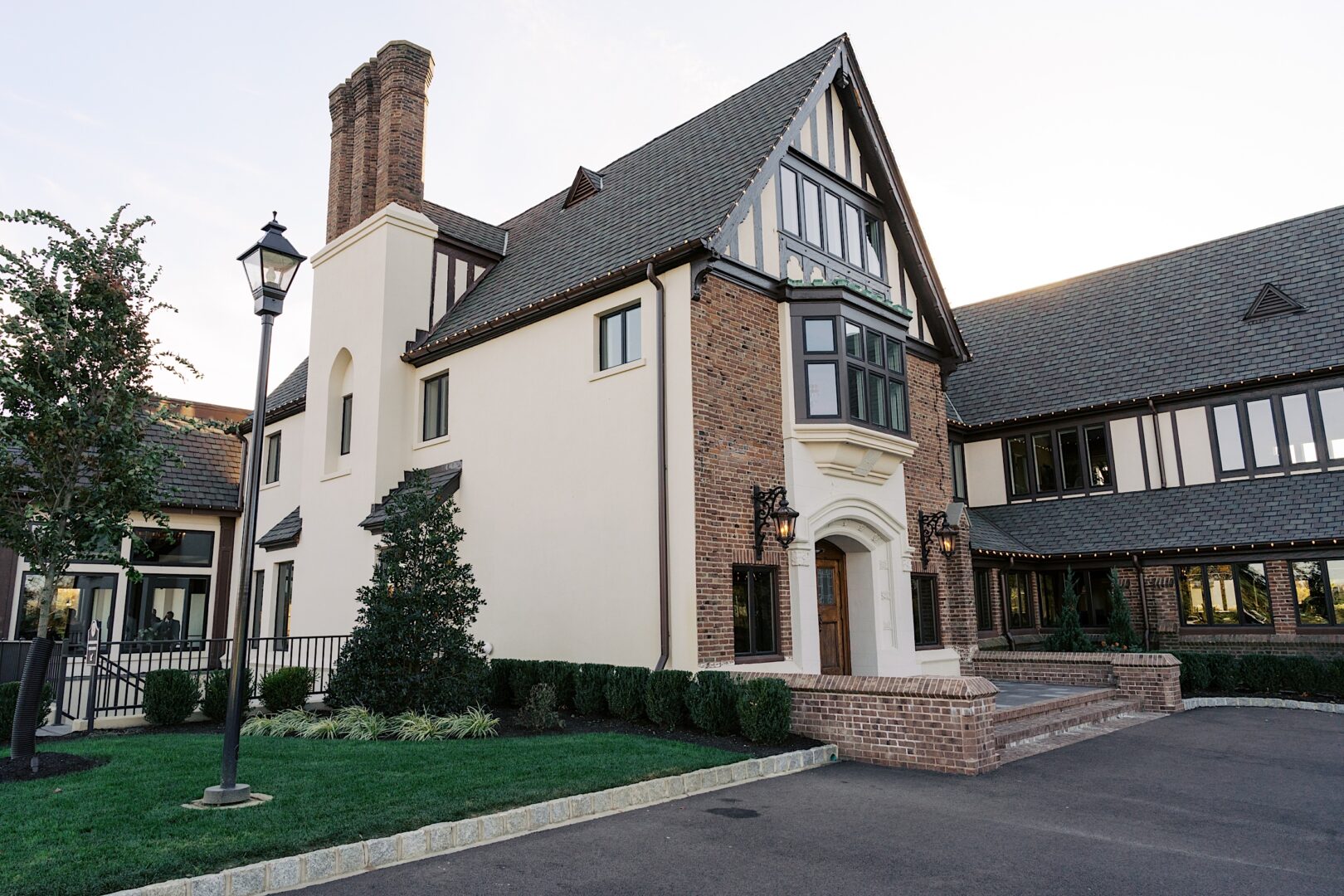 The Tilling House wedding offers a picturesque setting in a large Tudor-style brick and stucco home, featuring a steeply pitched roof, tall chimneys, and a manicured lawn.