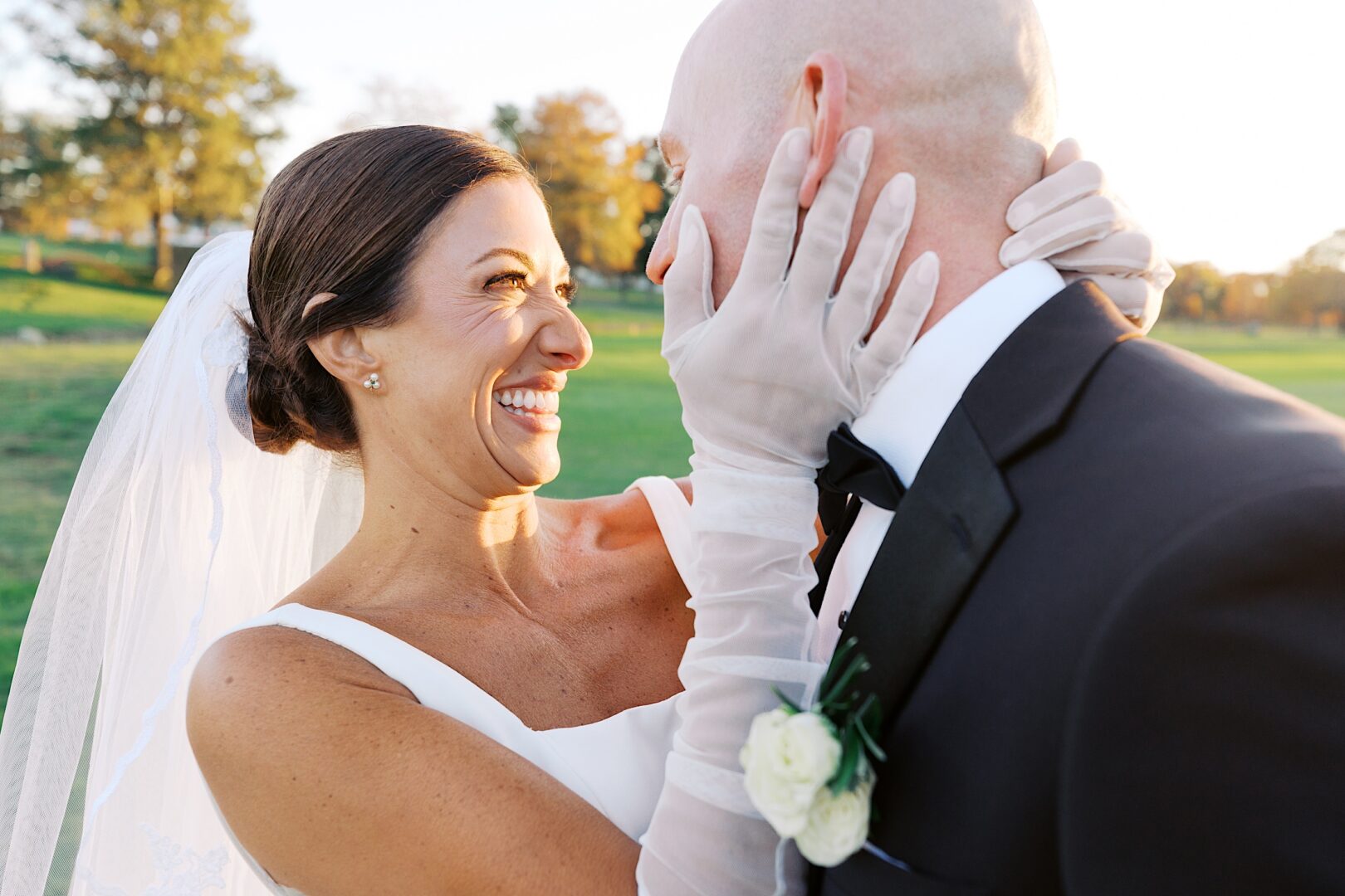 Bride and groom smiling at each other outdoors at The Tilling House wedding, with the bride wearing a veil and gloves, and the groom in a tuxedo with a boutonniere.