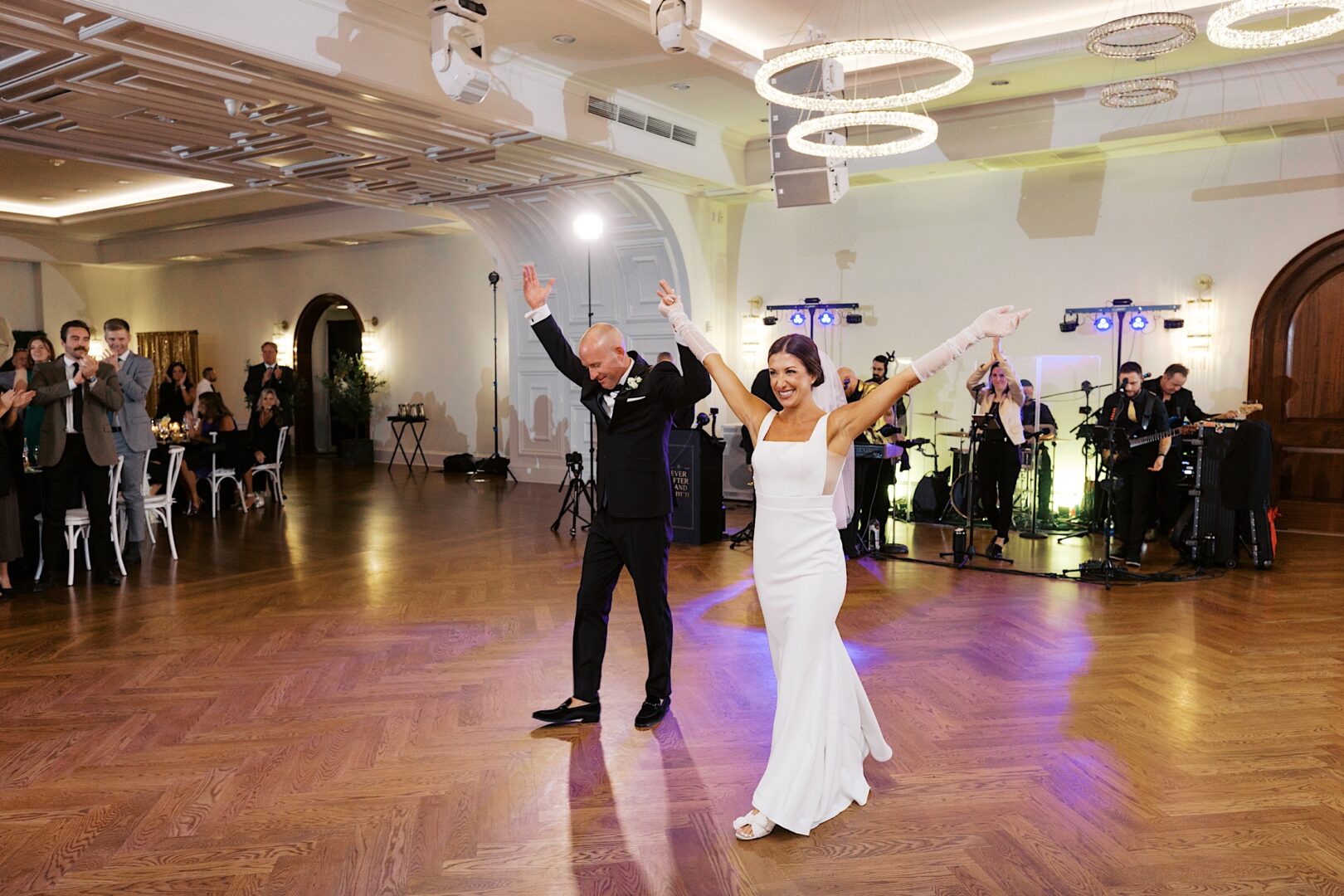 At The Tilling House wedding, a couple dances joyfully in a formal venue, surrounded by onlookers and musicians.