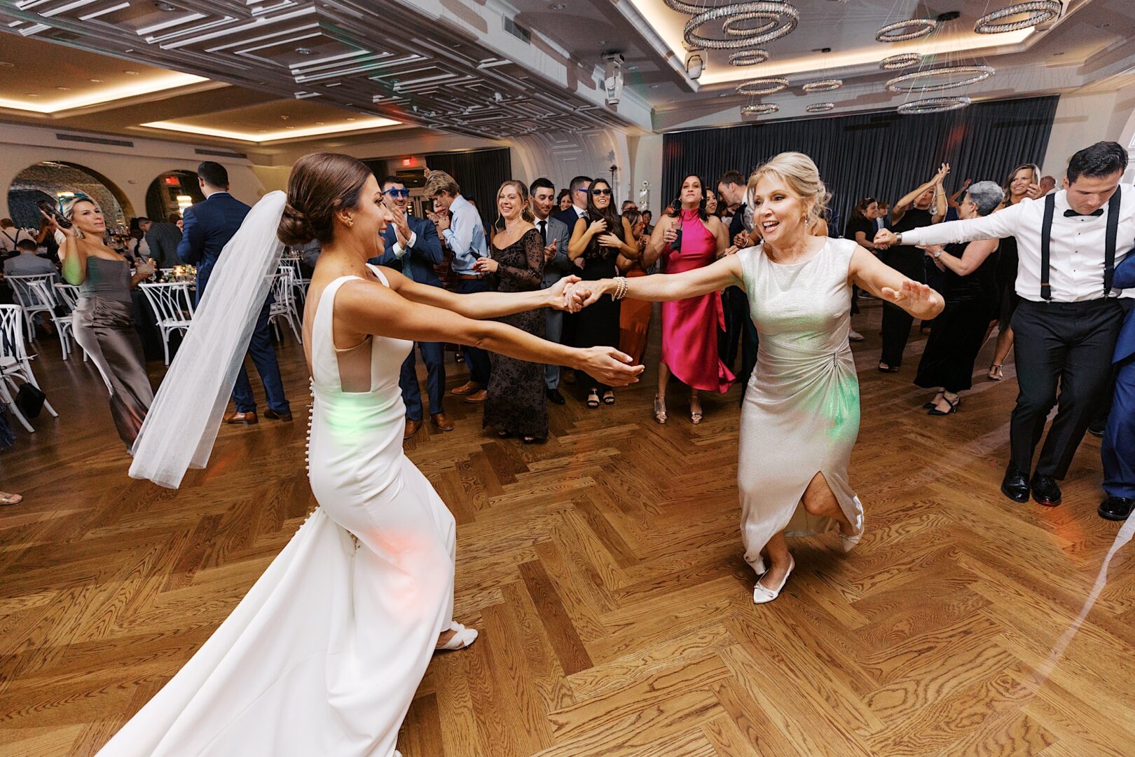 At The Tilling House wedding, a bride and a woman dance energetically on the wooden dance floor, surrounded by delighted guests.