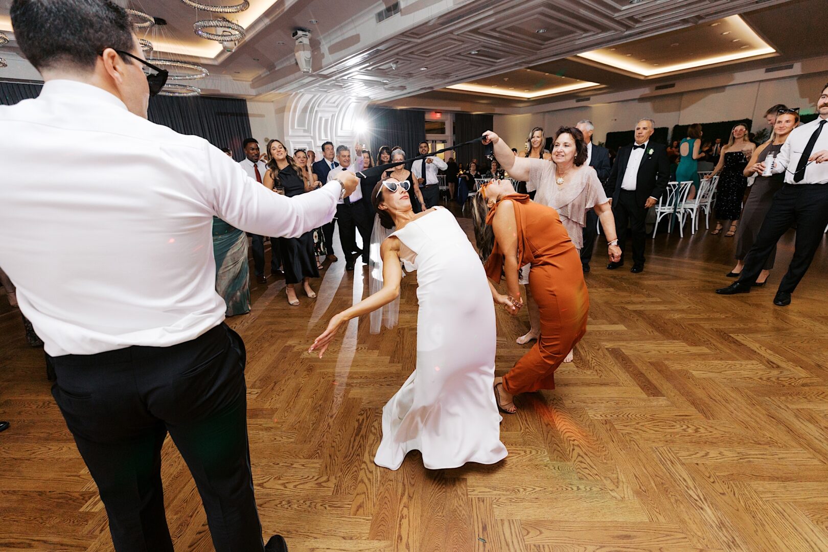 At The Tilling House wedding, guests are joyfully dancing and joining a lively limbo contest on the polished wooden floor, adding to the festive indoor celebration.