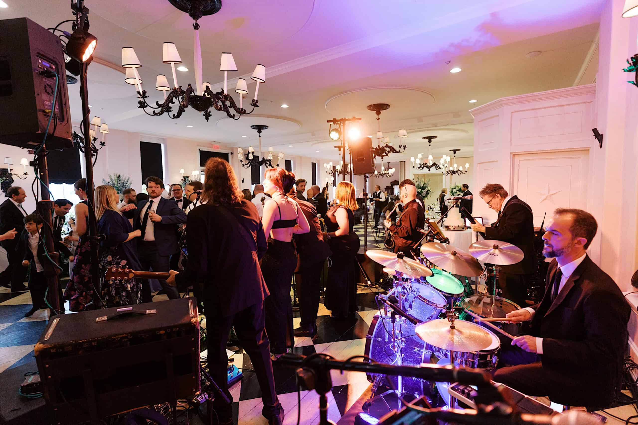 A live band performs on stage at a formal indoor event at a renowned New Jersey Beach Wedding Venue, while guests in formal attire mingle and socialize on a black-and-white checkered floor.