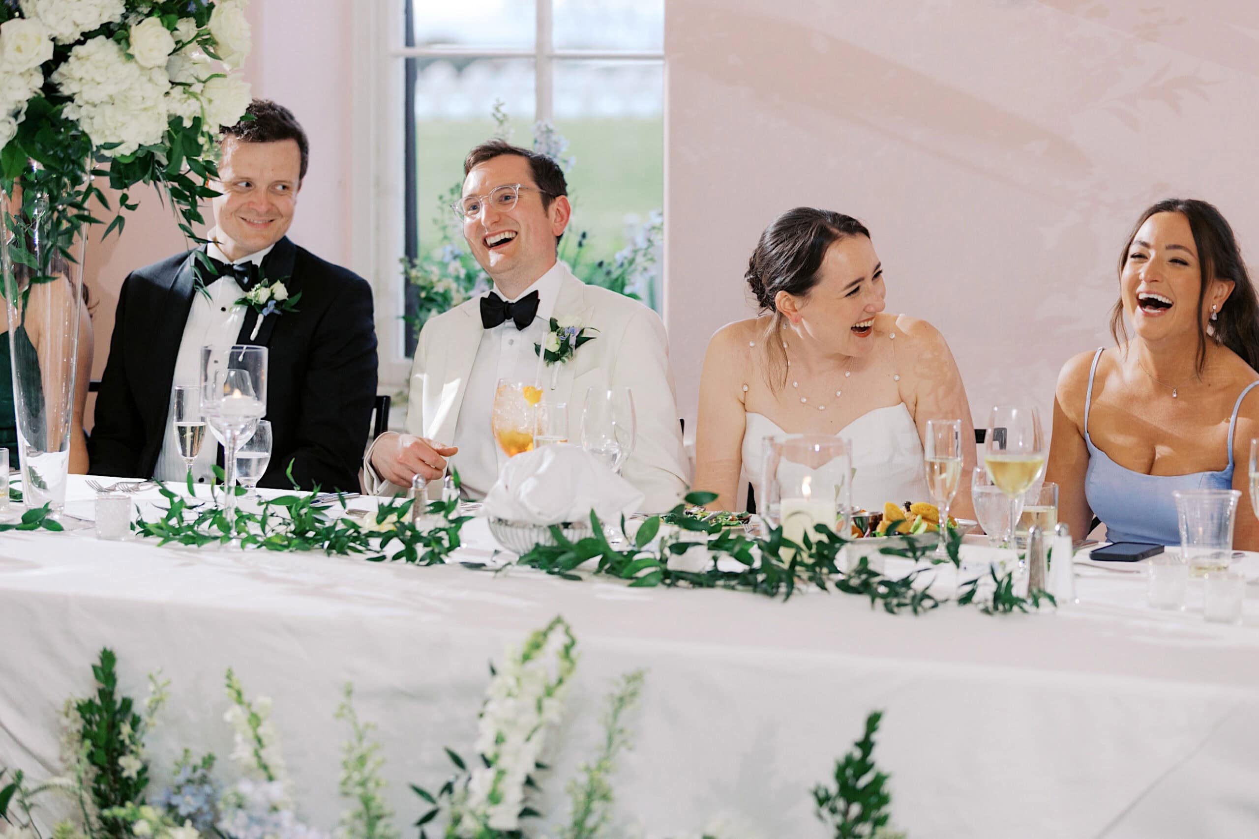 Four people dressed formally sit at a decorated table, smiling and laughing during what appears to be a wedding reception at a stunning New Jersey Beach Wedding Venue.