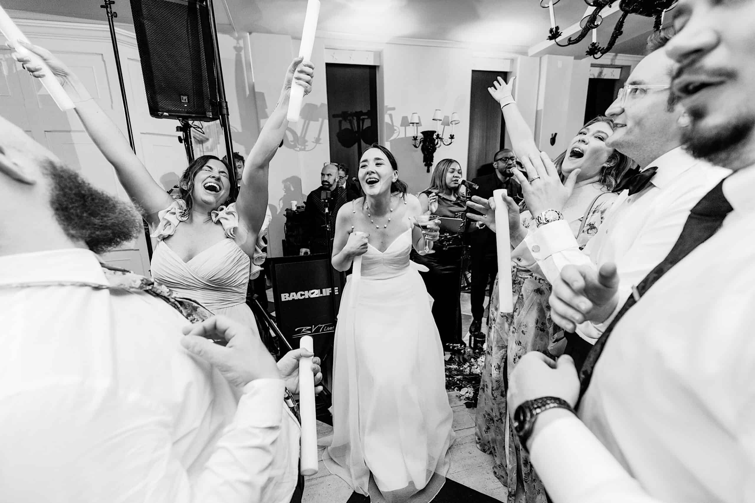 A group of people, including a bride in a white dress, celebrate and cheer together indoors at a lively New Jersey Beach Wedding Venue event.