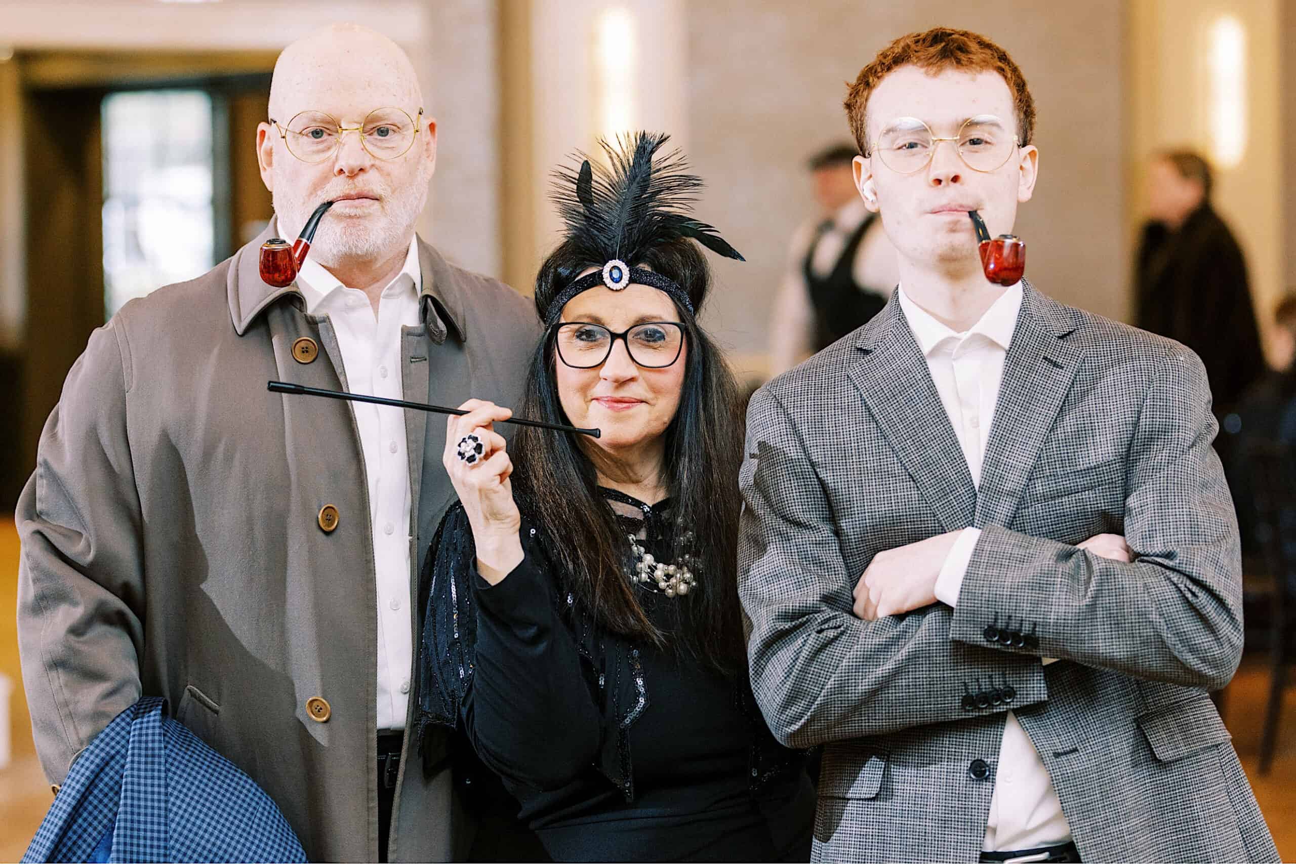 Three people posing indoors in costume: an older man in a trench coat with a pipe, a woman in Great Gatsby-inspired 1920s flapper attire for her Sweet 16, and a younger man in a checked suit, also holding a pipe.