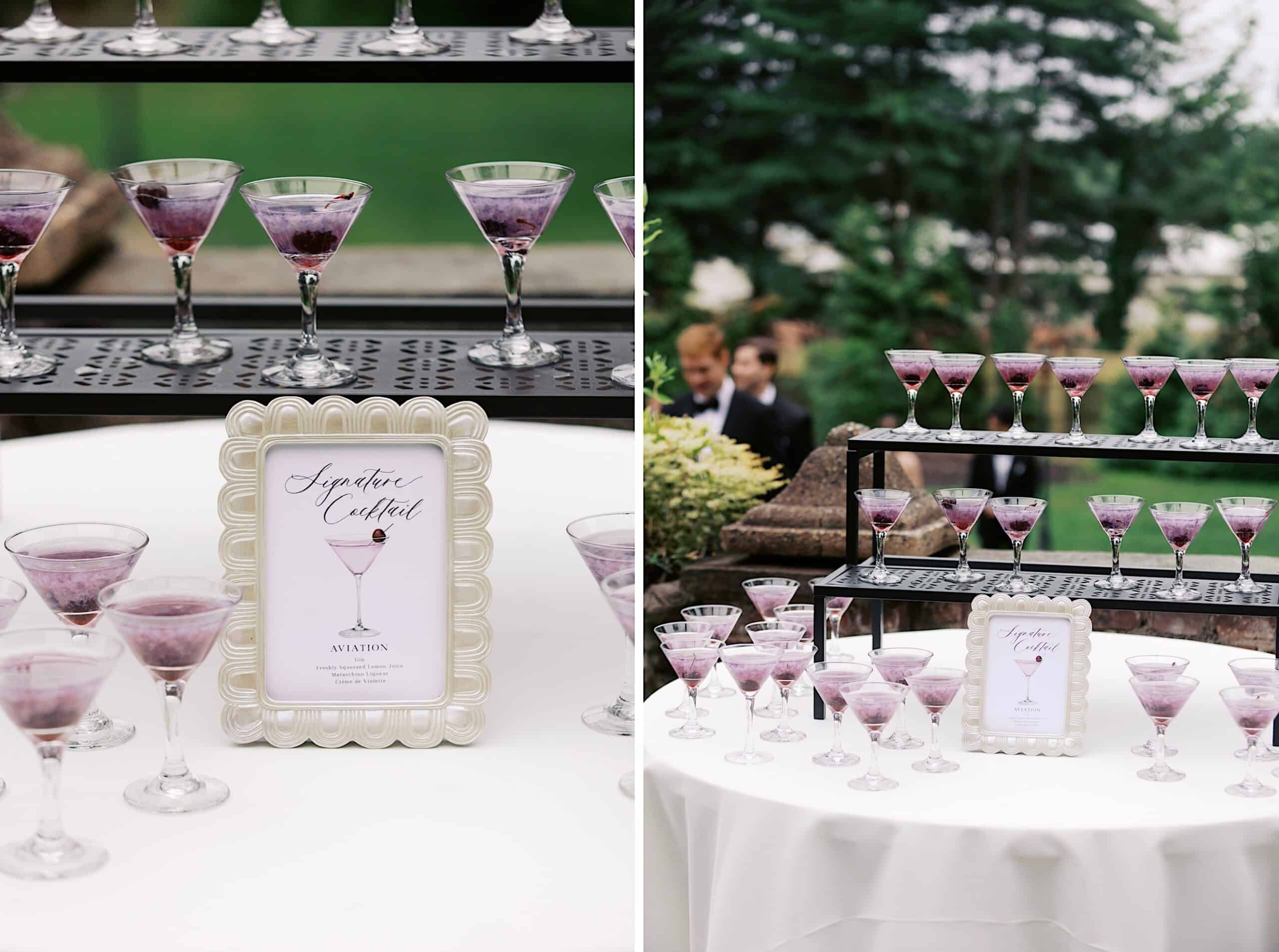 At a Wedding at Aldie Mansion, several purple cocktails in martini glasses are displayed on a round table and black shelves outdoors, with a framed "Signature Cocktail Aviation" sign on the table.