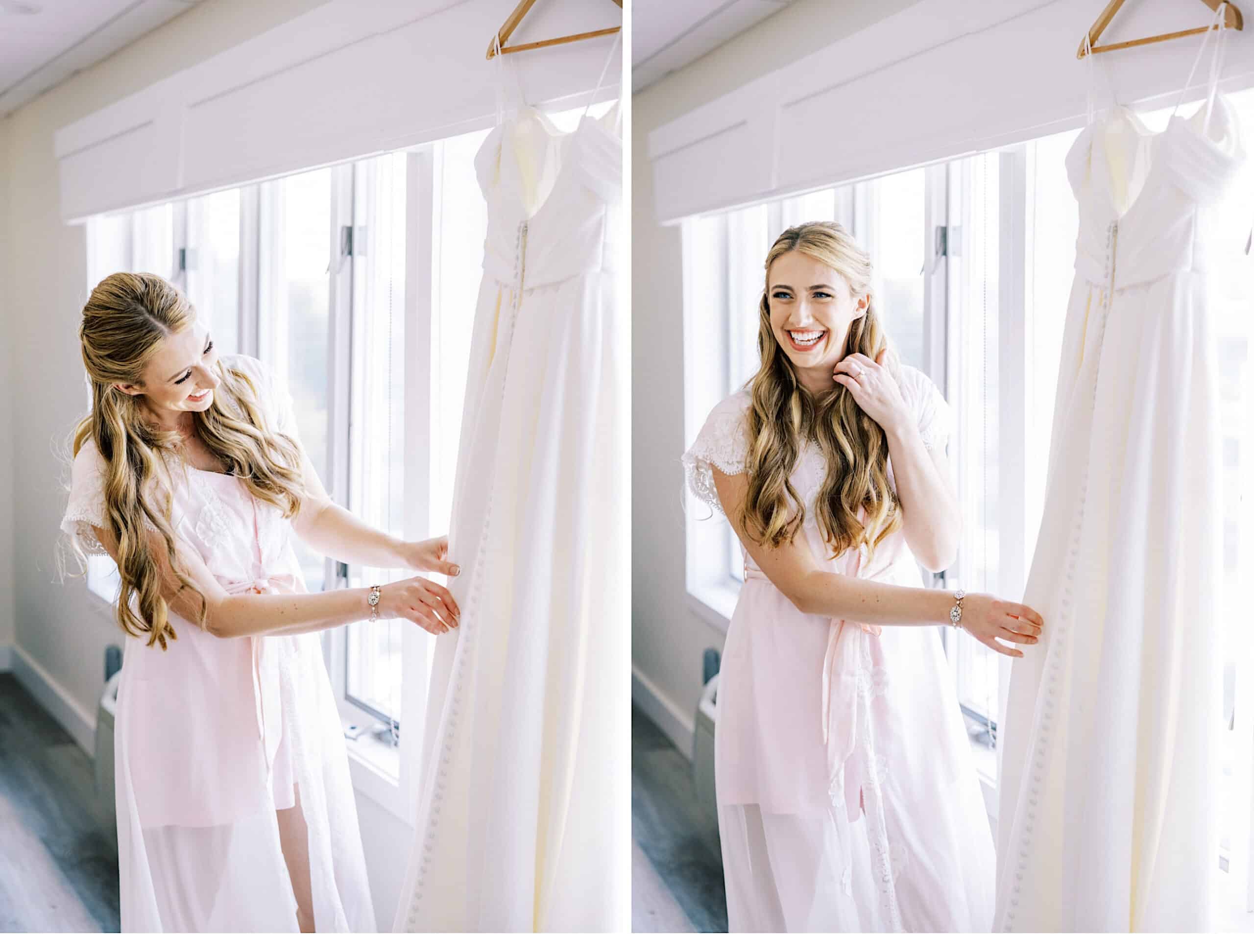 A woman in a light pink robe smiles while standing next to a white wedding dress hanging by a window, capturing the joyful anticipation of her Montreal Beach Resort Wedding in a bright room.