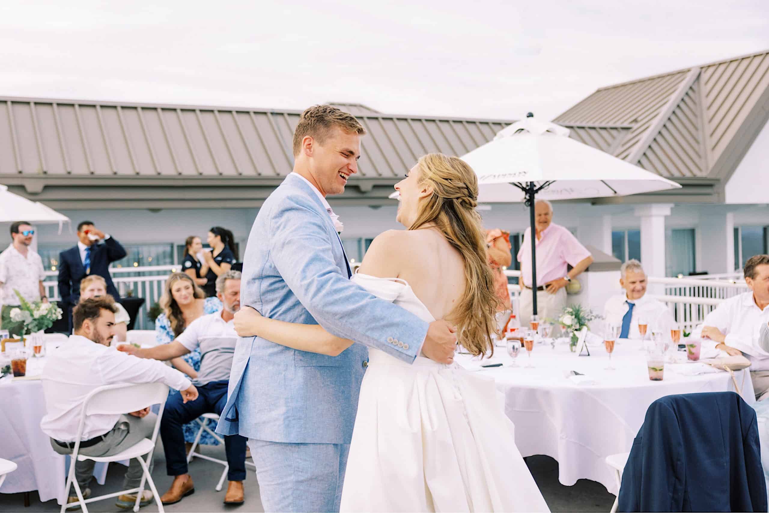 At a Montreal Beach Resort Wedding, a bride and groom dance together outdoors at their reception, surrounded by seated guests at round tables under umbrellas.
