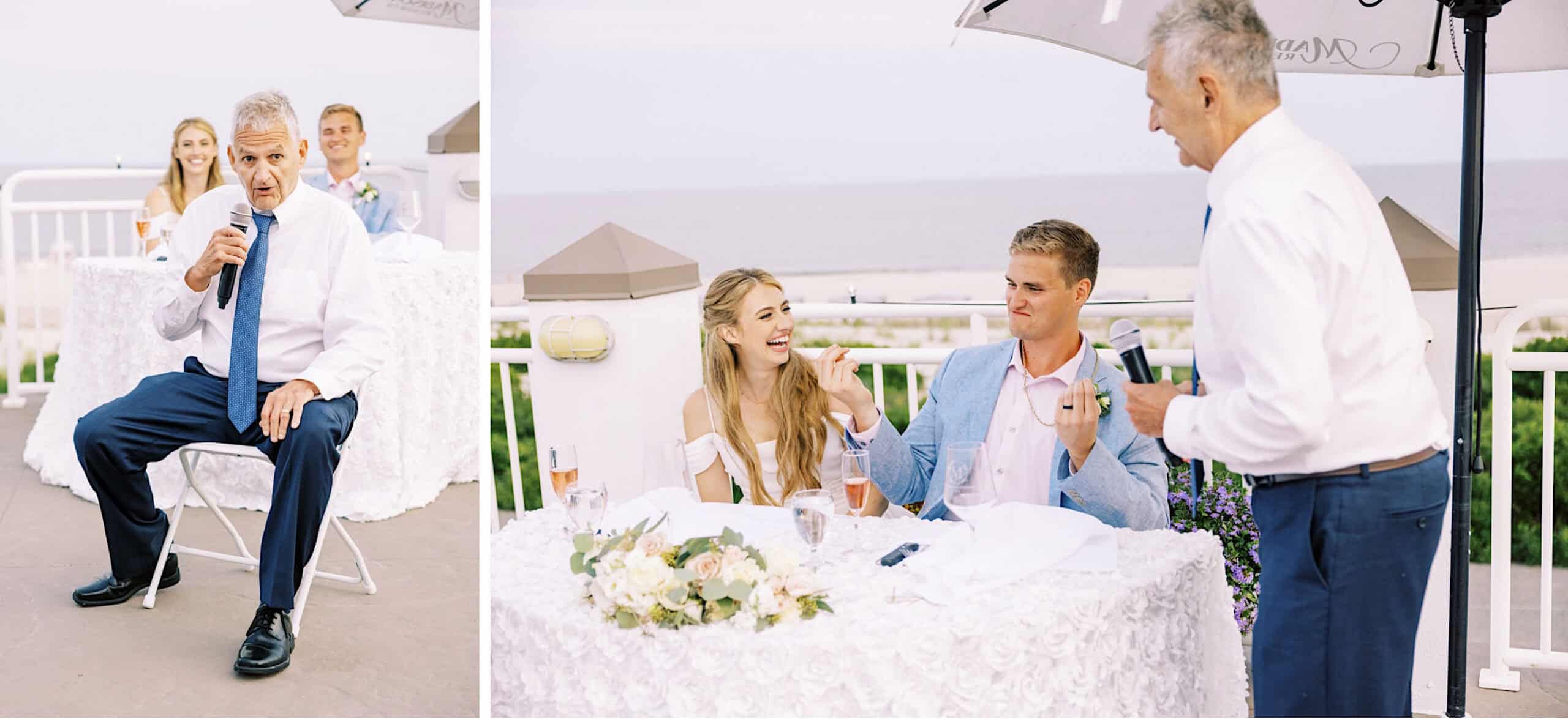 A man in a white shirt and blue tie gives a speech with a microphone at an outdoor Montreal Beach Resort Wedding as a couple sits at a table, smiling and listening.