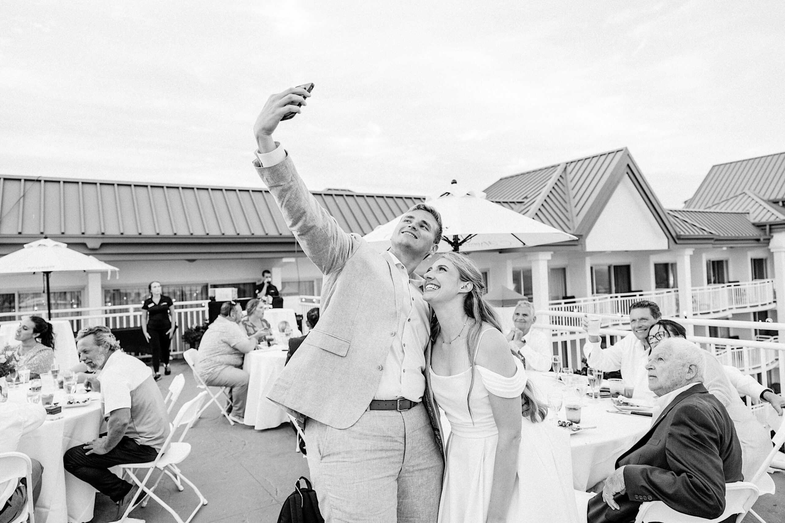 A couple takes a selfie together at their Montreal Beach Resort wedding, with guests seated at tables in the background.