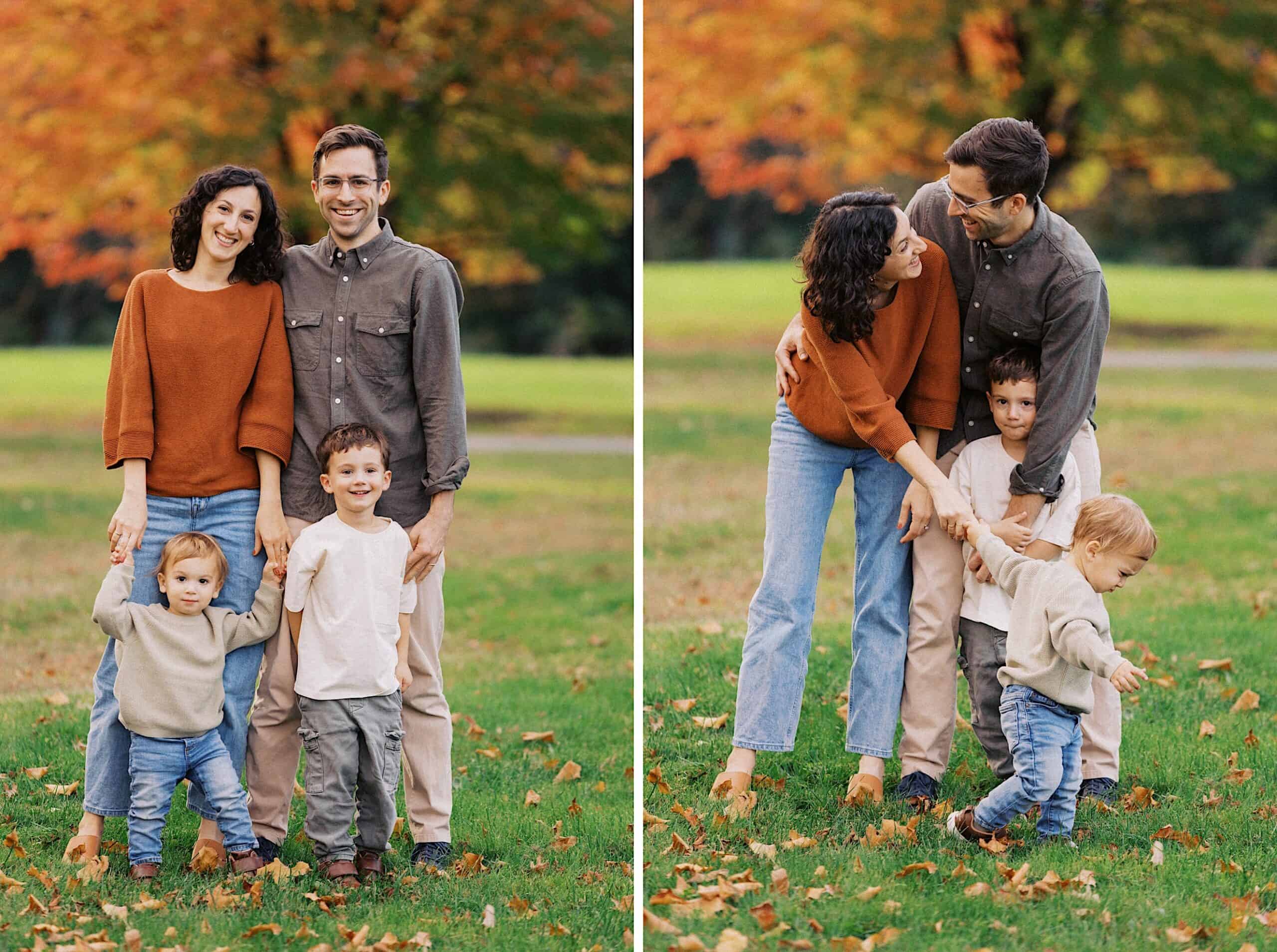 A family of four stands together outdoors in autumn; the parents and two young children pose and interact on green grass with orange trees in the background.