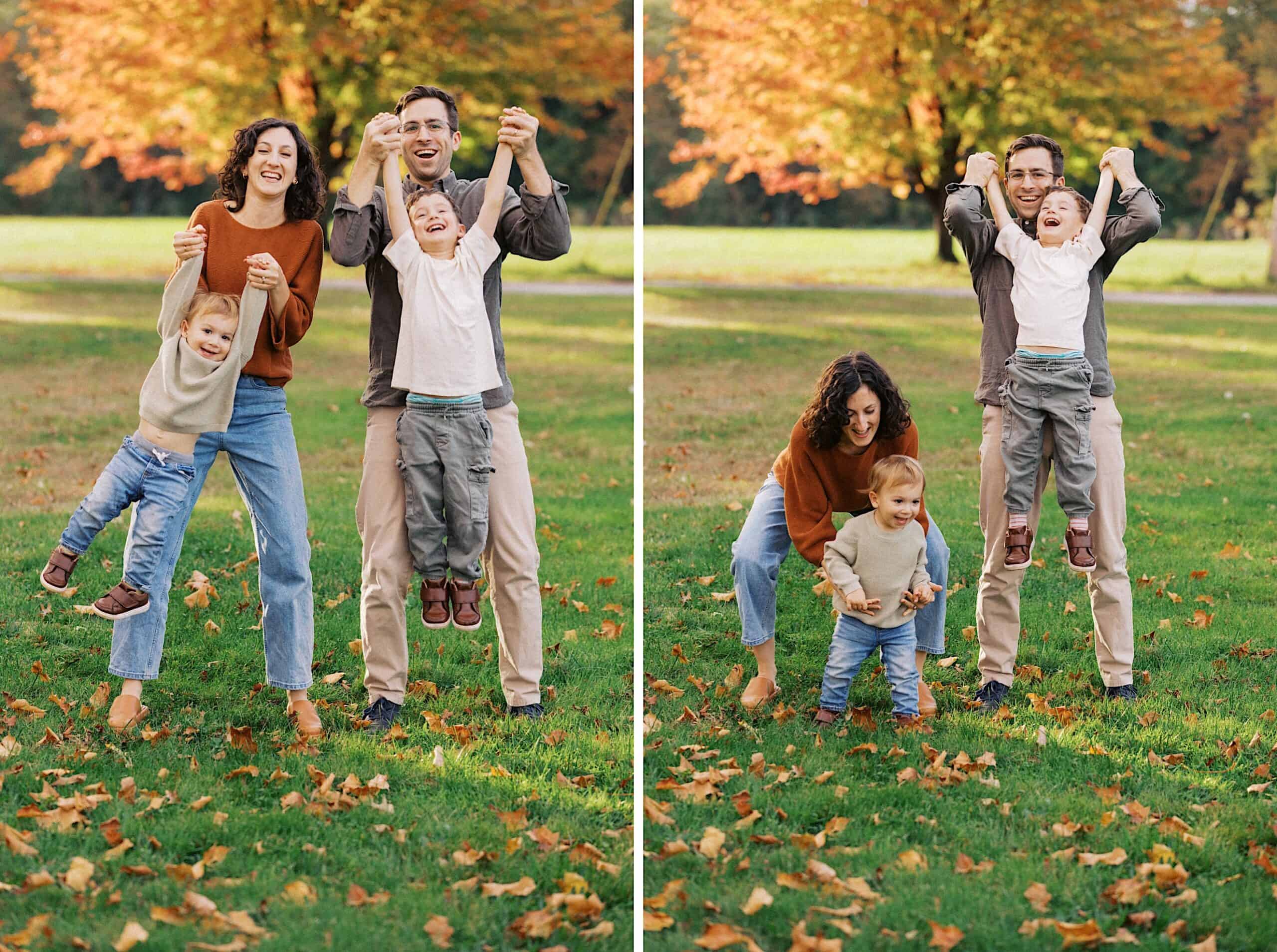 Two adults and two children play together outside on green grass with autumn leaves, lifting and swinging the children in a park setting with colorful trees in the background.
