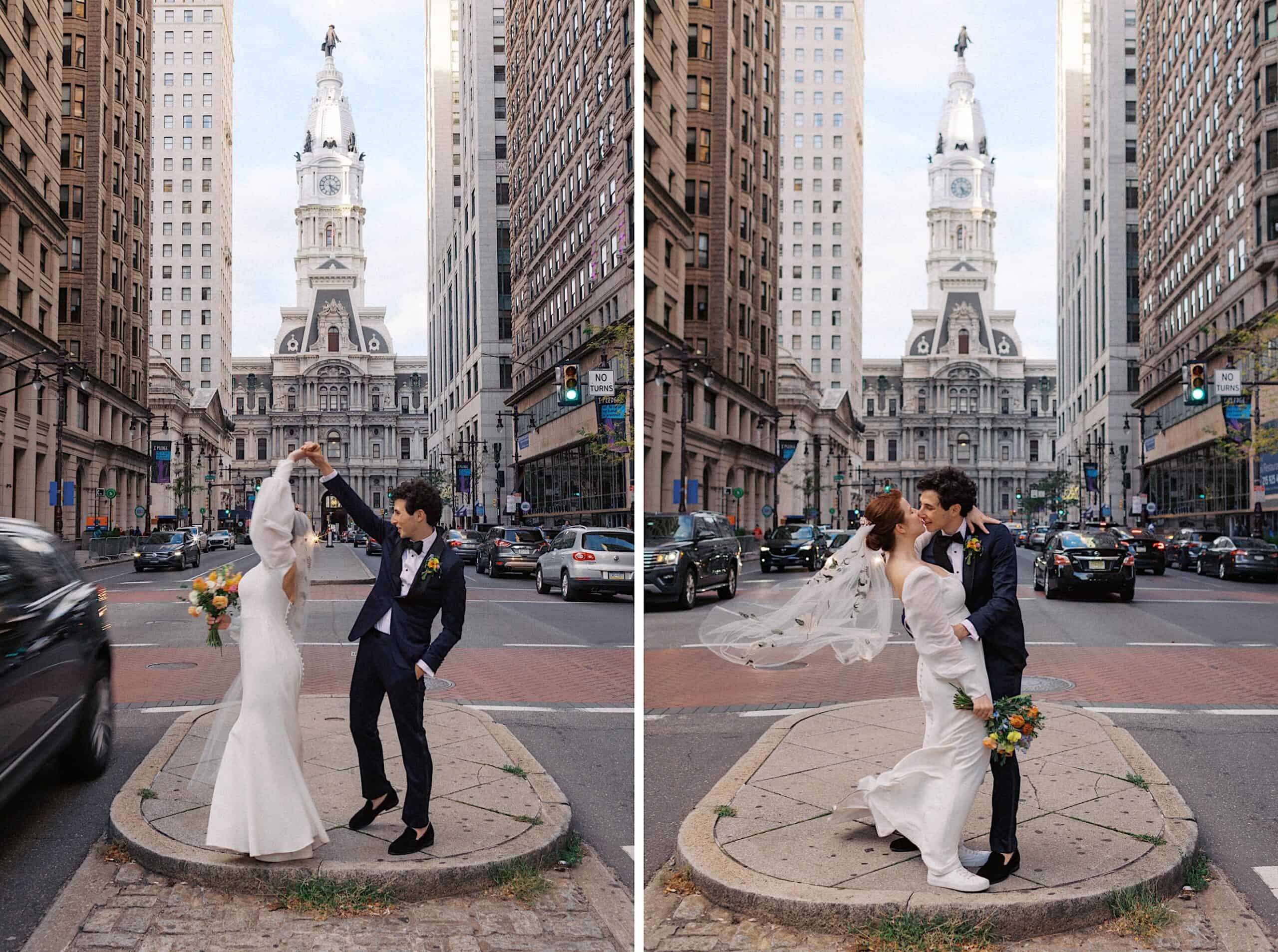 A bride and groom pose and dance on a traffic island in front of a historic building, surrounded by tall city buildings and cars.